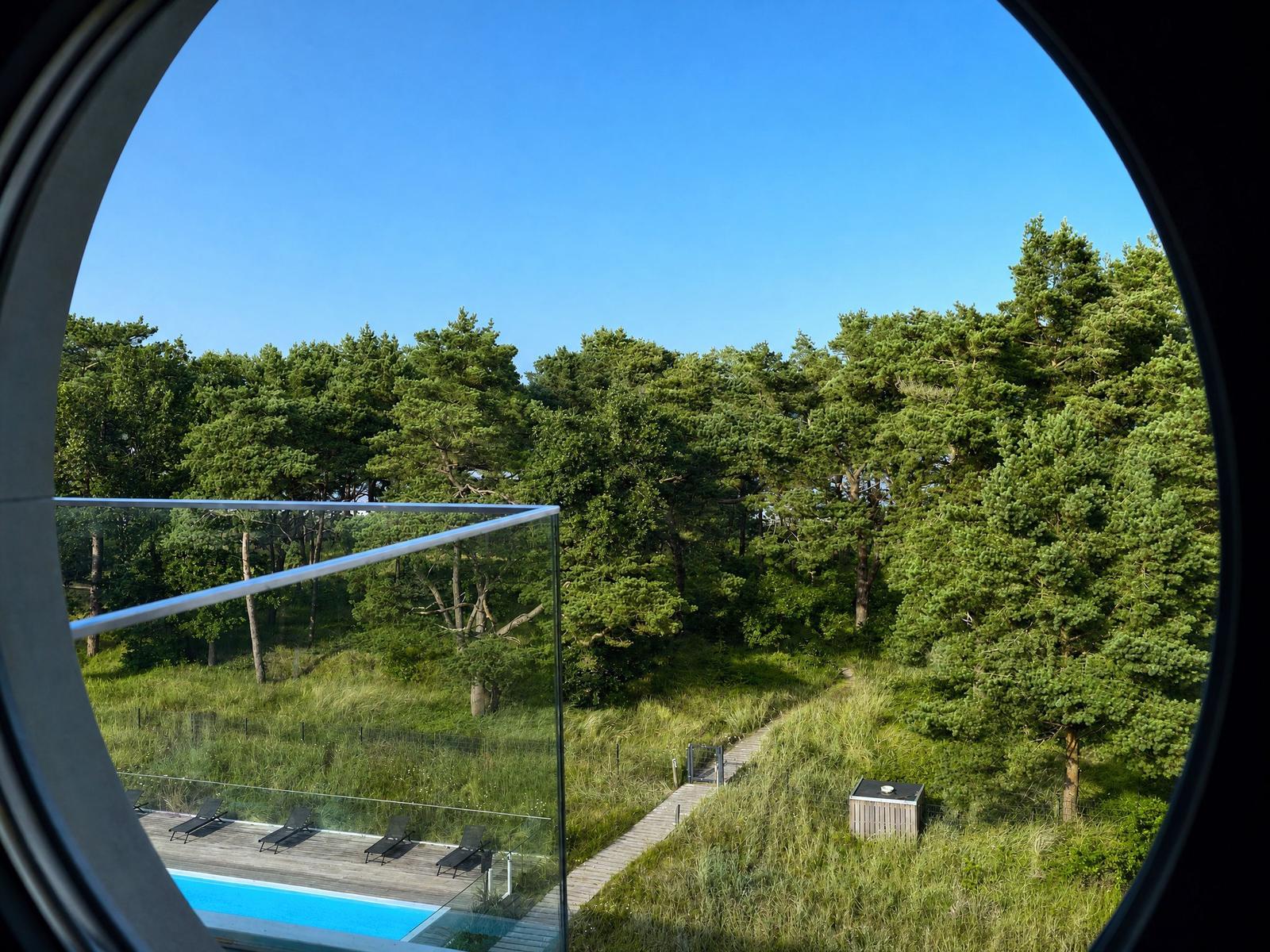 Rundes Fenster zeigt Poolbereich und Wald