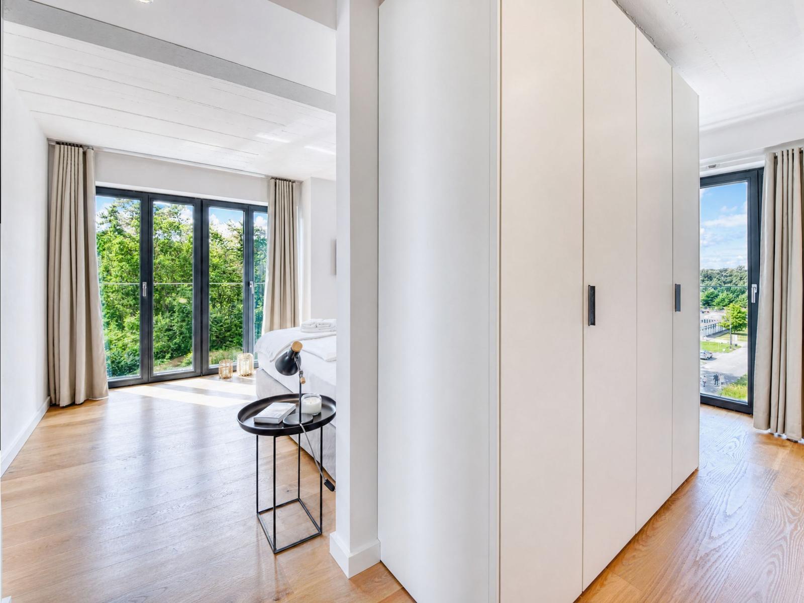 Schlafzimmer mit großem Fenster, Holzboden und Kleiderschrank.