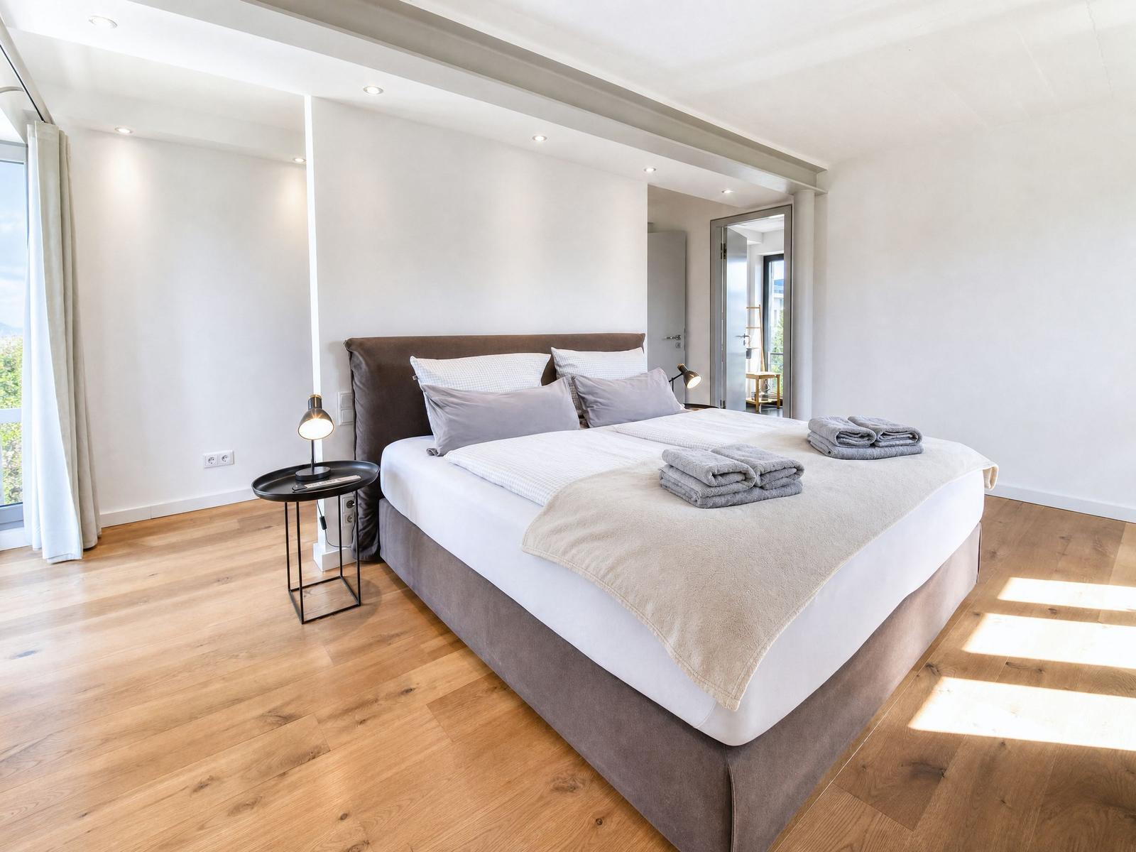 Ein Schlafzimmer mit einem großen Bett, Holzboden und einem Nachttisch mit Lampe.