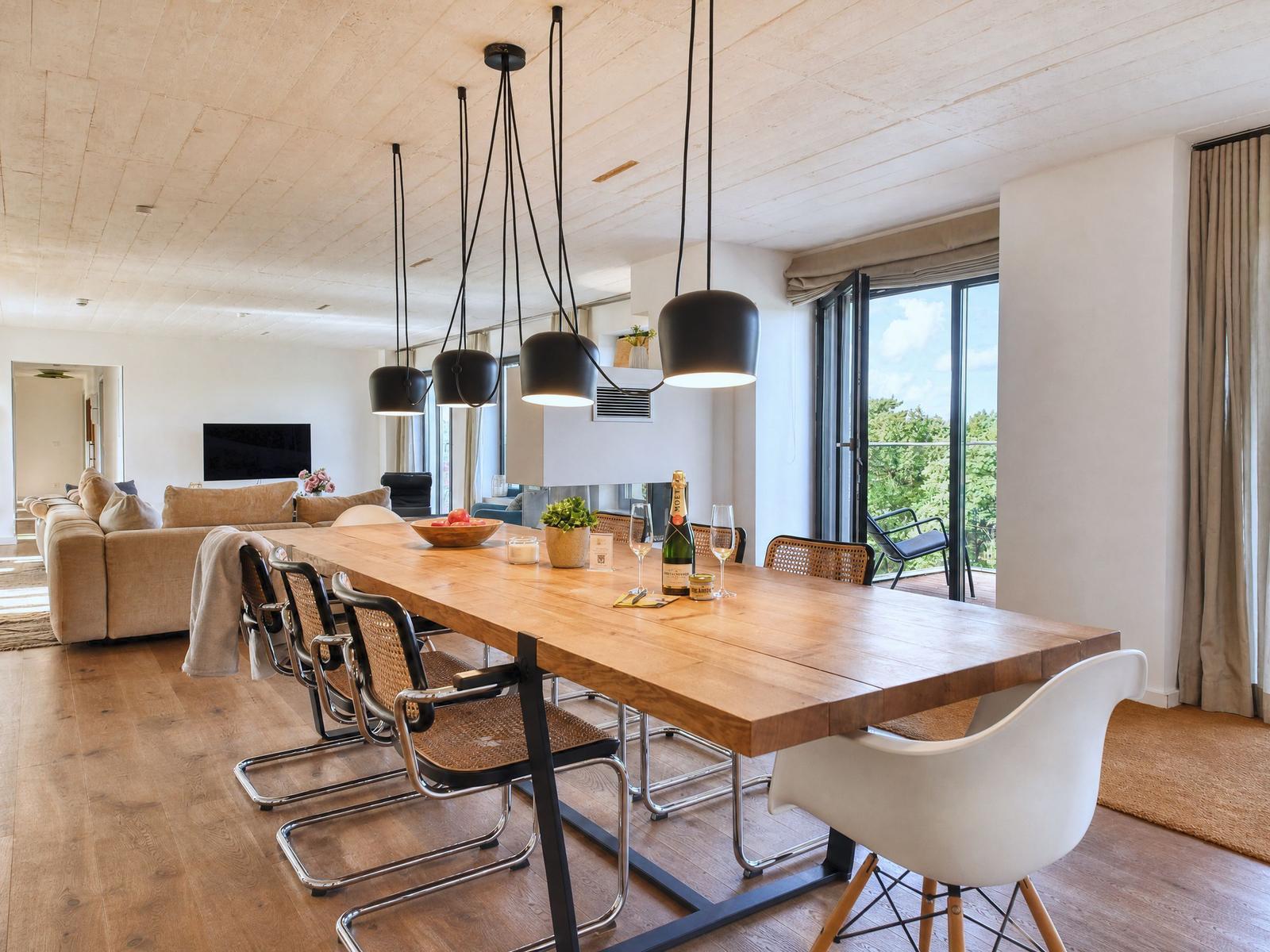Essbereich mit langem Holztisch und Stühlen, großes Fenster mit Blick auf Balkon.