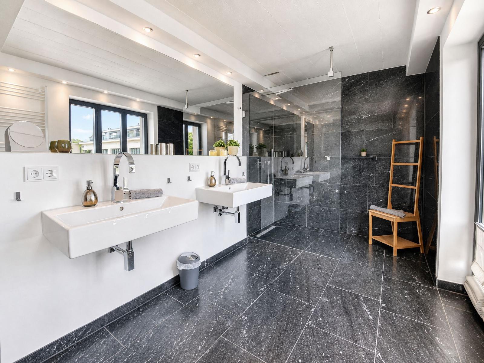Dusche mit Glaswand, zwei Waschbecken und schwarze Fliesen