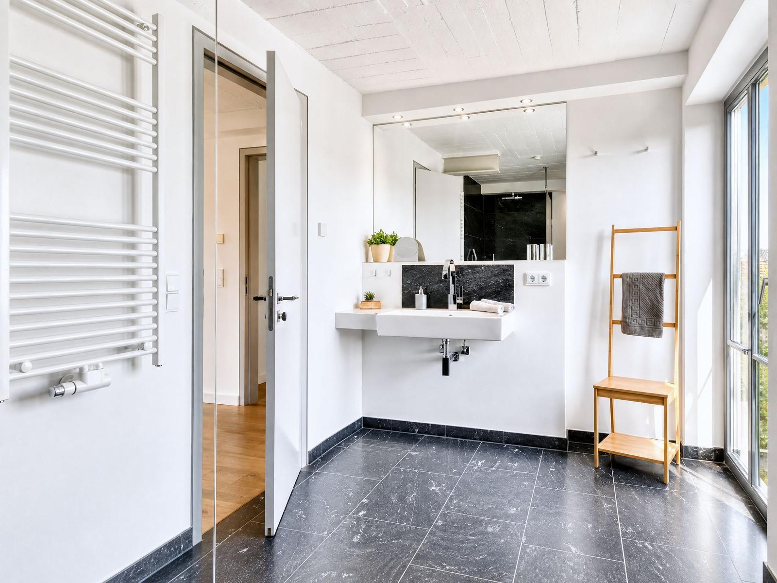 Badezimmer mit Waschbecken, Spiegel und Holzhandtuchständer. Schwarze Fliesen und weißer Wand.