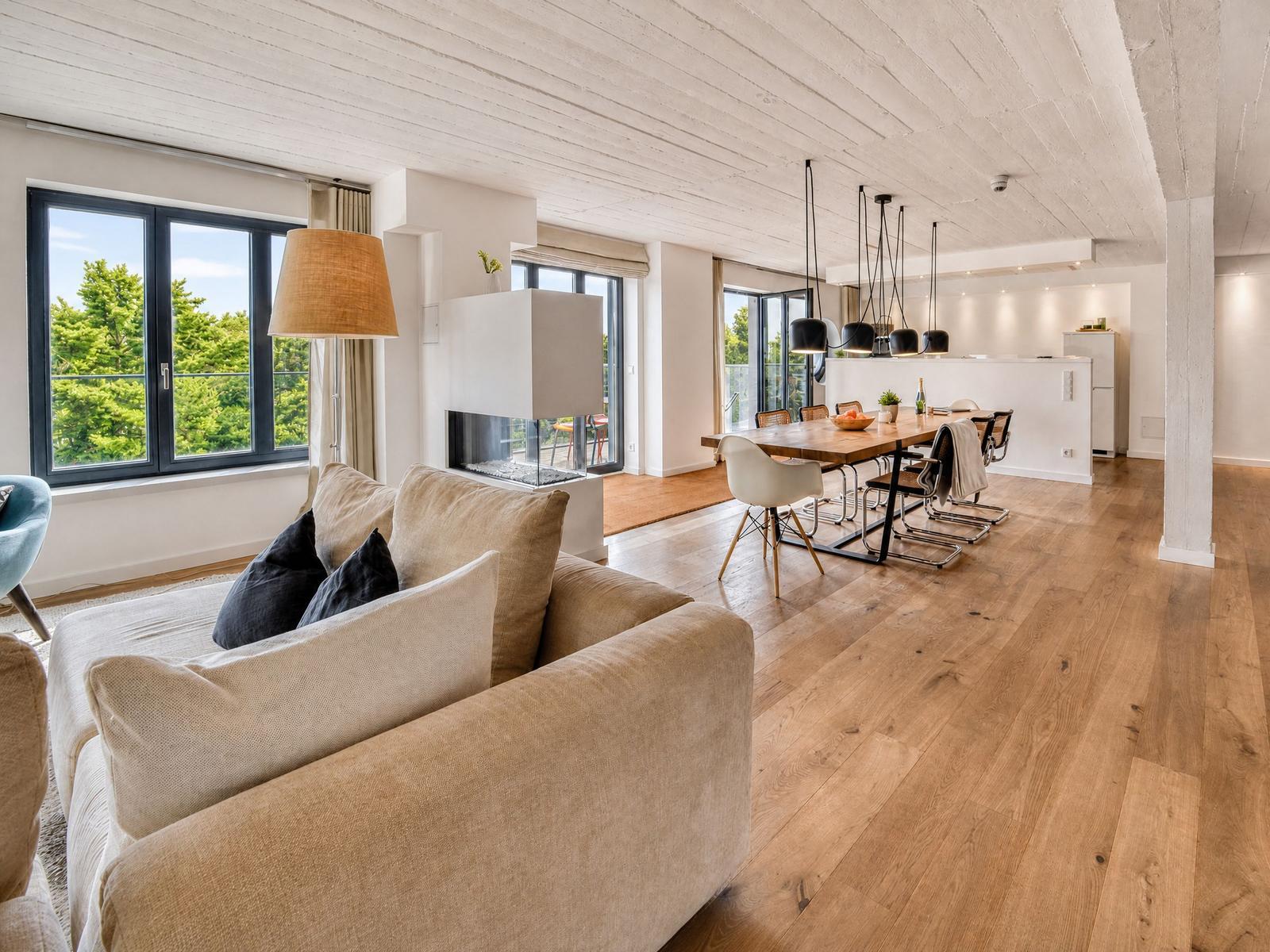 Wohn- und Essbereich mit Holzboden, großen Fenstern und moderner Einrichtung.
