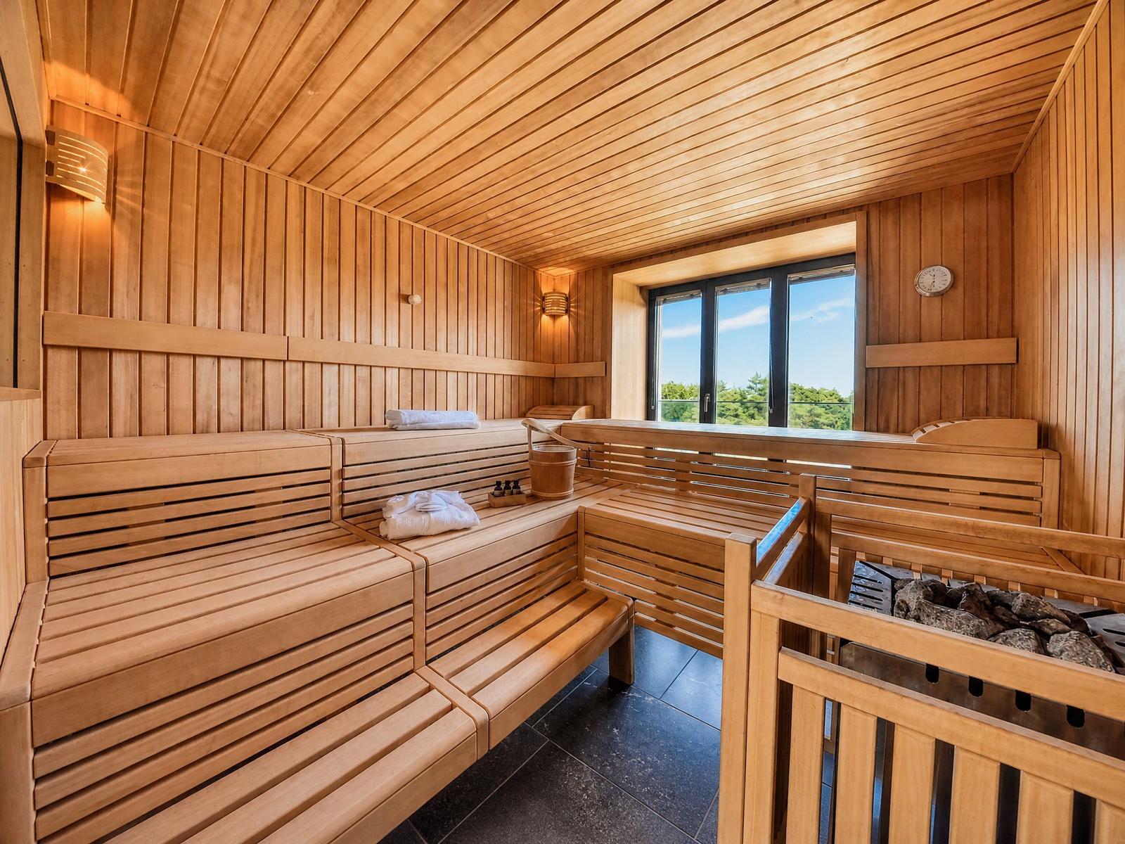 Holzsauna mit Sitzbänken, Fenster und Ofen. Handtuch und Eimer sind vorhanden.