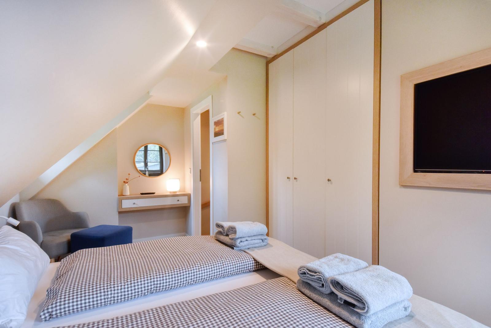 Schlafzimmer mit Doppelbett, Kleiderschrank und Fernseher an der Wand.