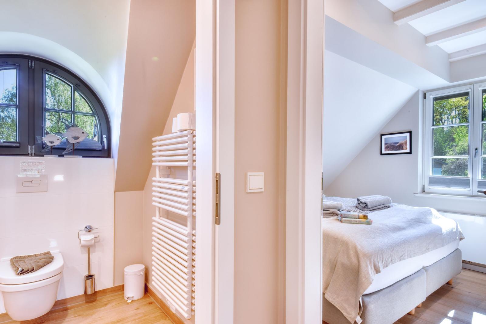 Schlafzimmer mit Bett und Fenster. Nebenraum mit Toilette und Heizkörper.