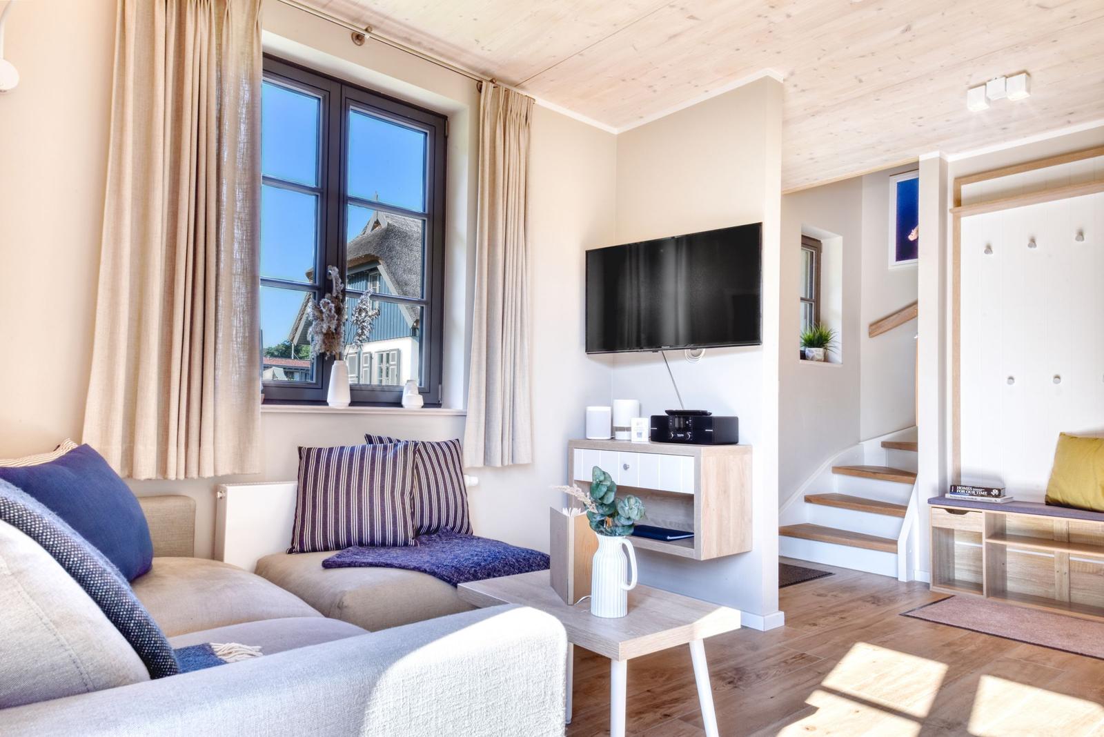 Wohnzimmer mit Sofa, Fernseher und Blick auf Dachhäuser.