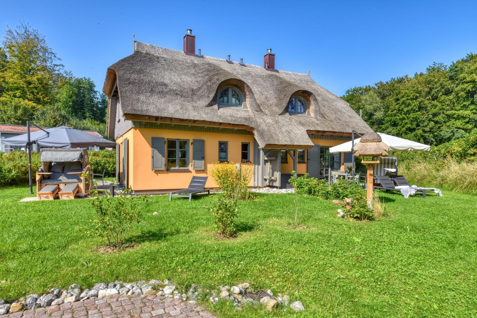 Haus mit Strohdach, Garten, Sonnenliegen und Terrasse.