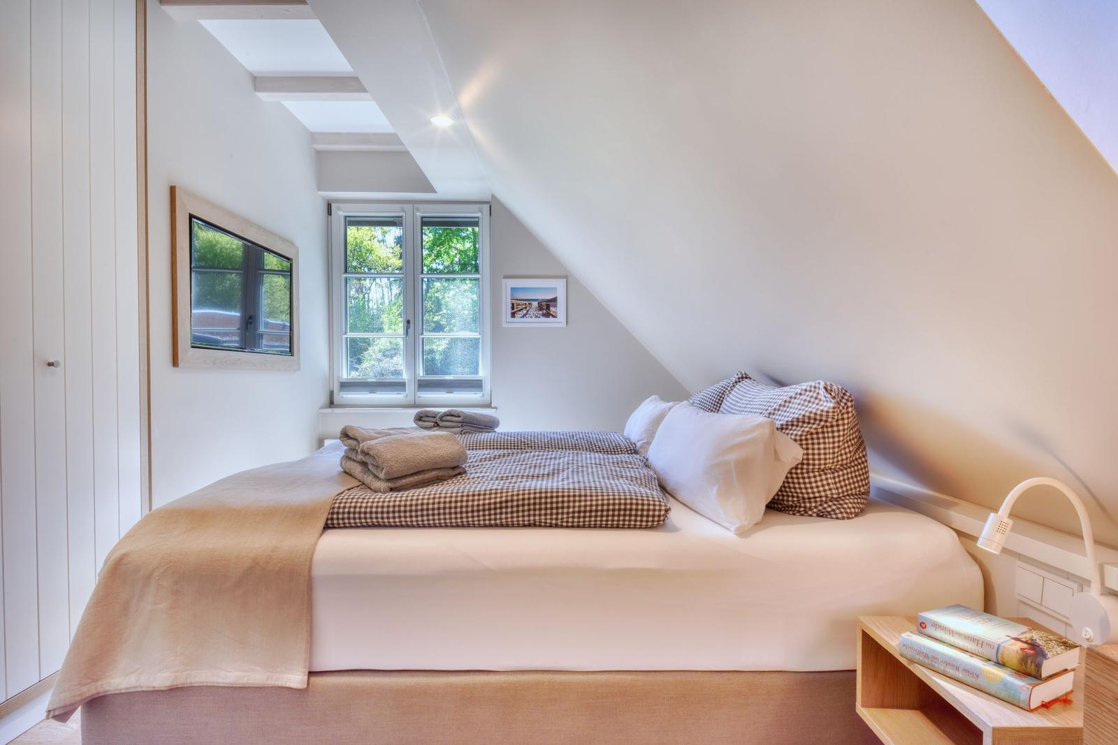 Schlafzimmer mit Dachschrägen, Bett, Fenster und Nachttisch.