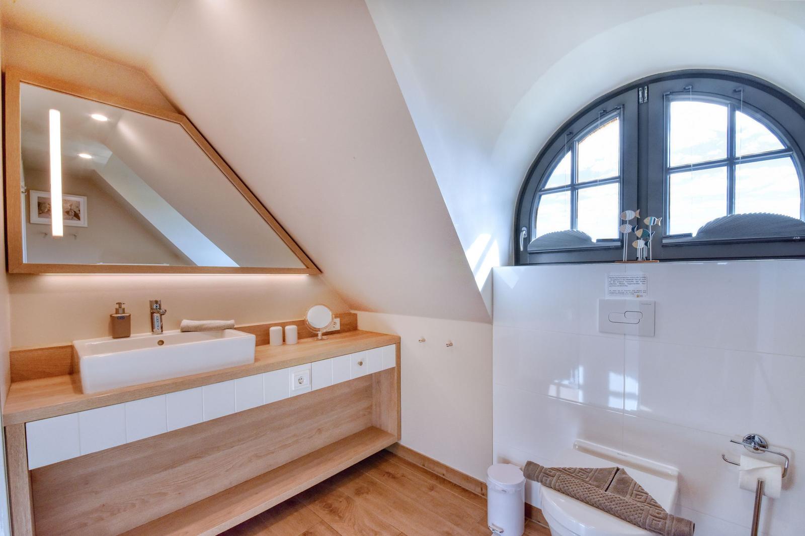 Badezimmer mit Waschtisch, Spiegel und Bogenfenster.