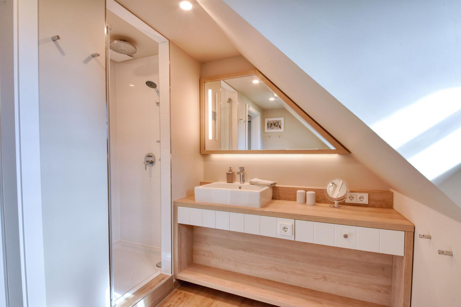 Badezimmer mit Dusche, Waschbecken und Spiegel unter Dachschrägen.