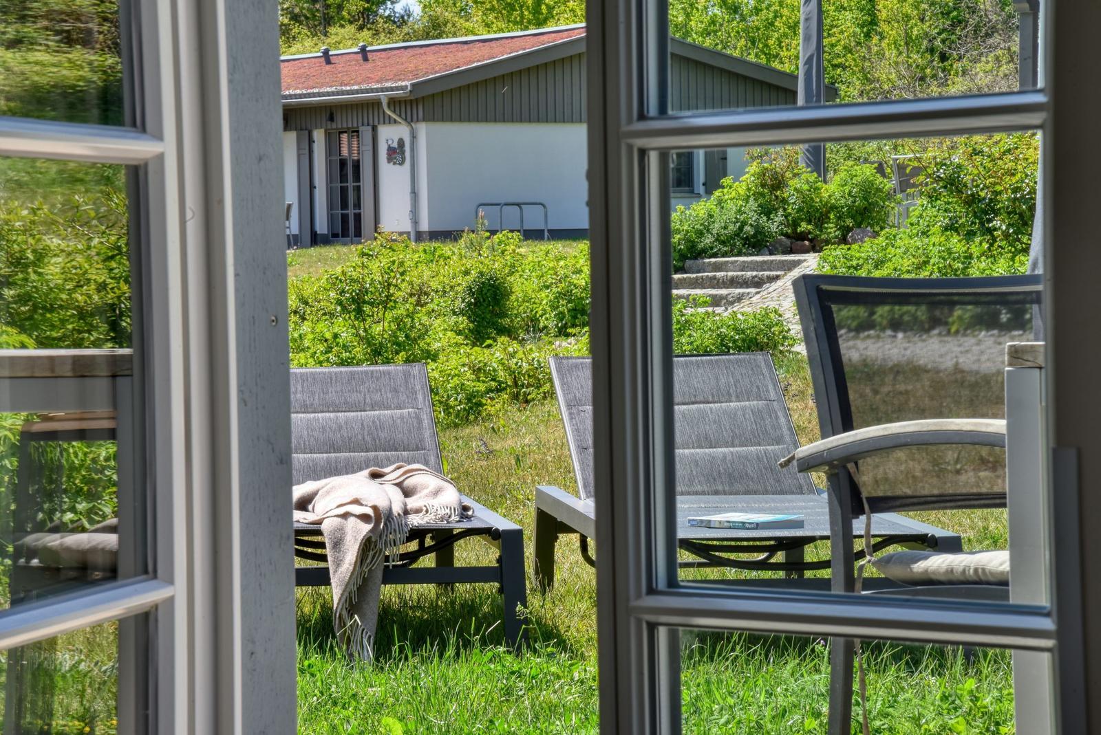 Von innen betrachtet, zeigt das Bild einen Garten mit Liegestühlen und einem Haus im Hintergrund.