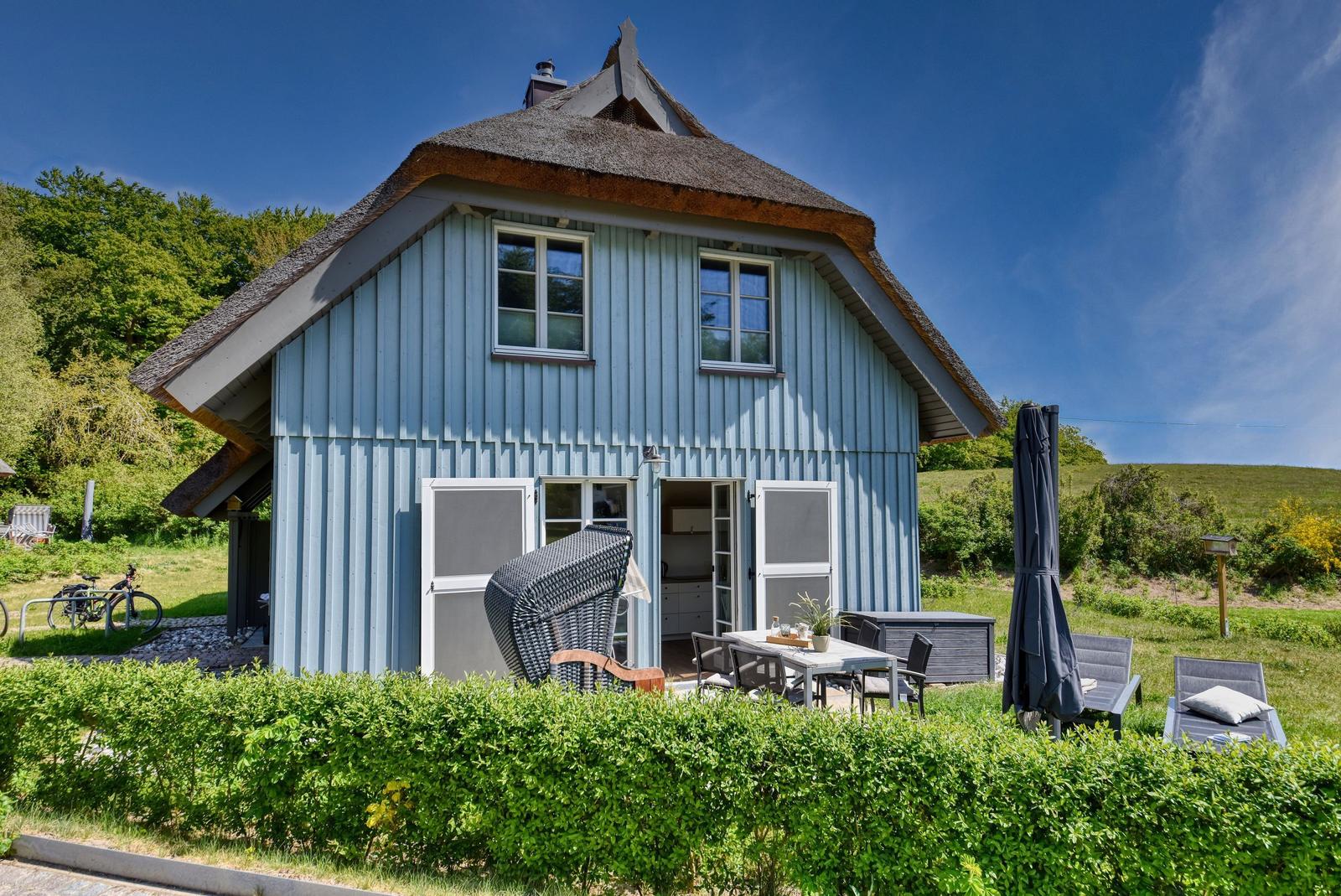 Ein blaues Holzhaus mit Strohdach und Terrasse im Freien.