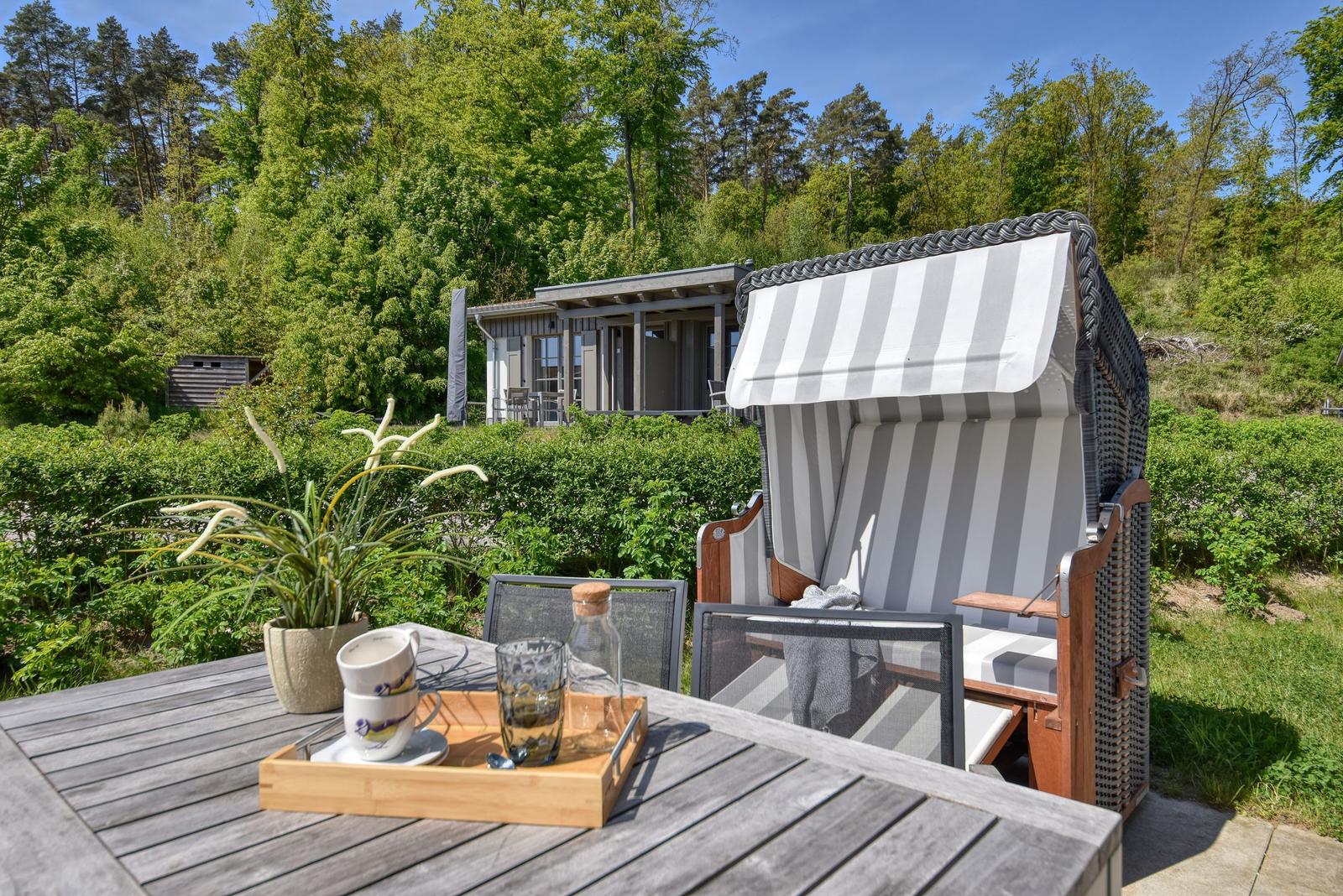 Terrasse mit Liegestuhl und Tisch. Im Hintergrund modernes Haus und Wald.