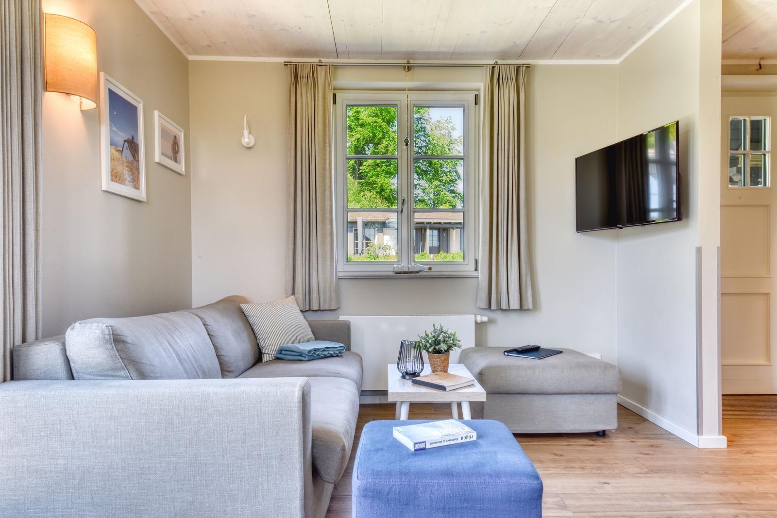 Wohnzimmer mit Sofa, Fernseher und Fenster mit Blick auf Bäume.