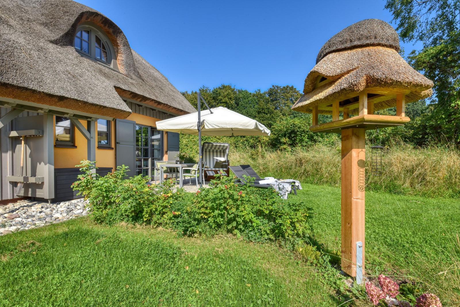 Haus mit Strohdach, Gartenbereich mit Sonnenschirm und Liegestühlen, Vogelhaus mit Strohdach.