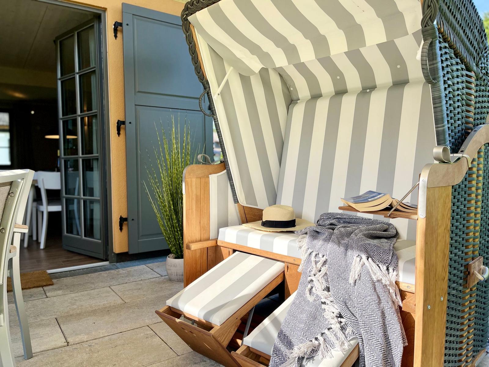 Strandkorb mit Streifenbezug, Schal und Hut auf Terrasse vor Haus.