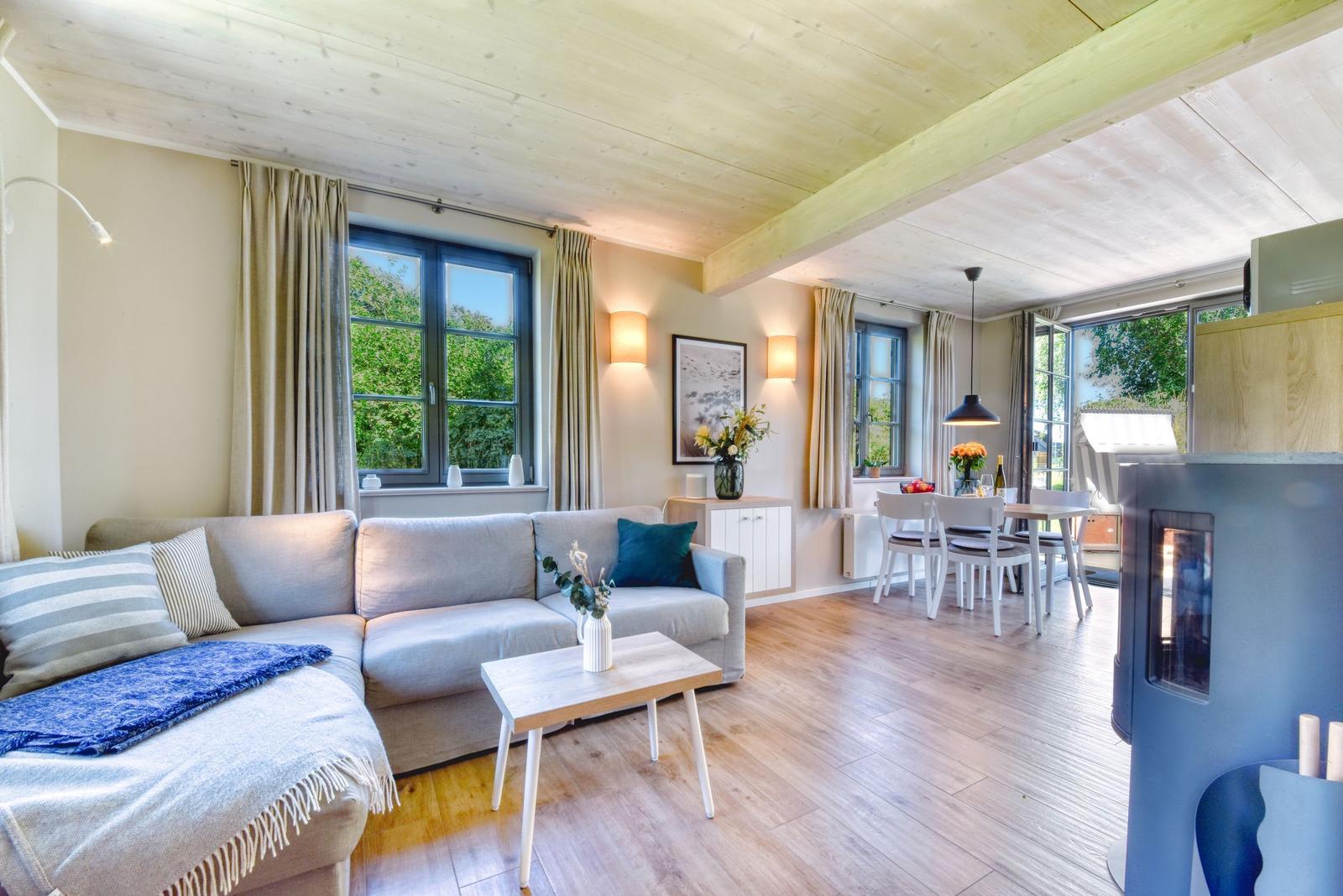 Wohn- und Essbereich mit Sofa, Tisch und Fenstern. Holzdecke und Boden.