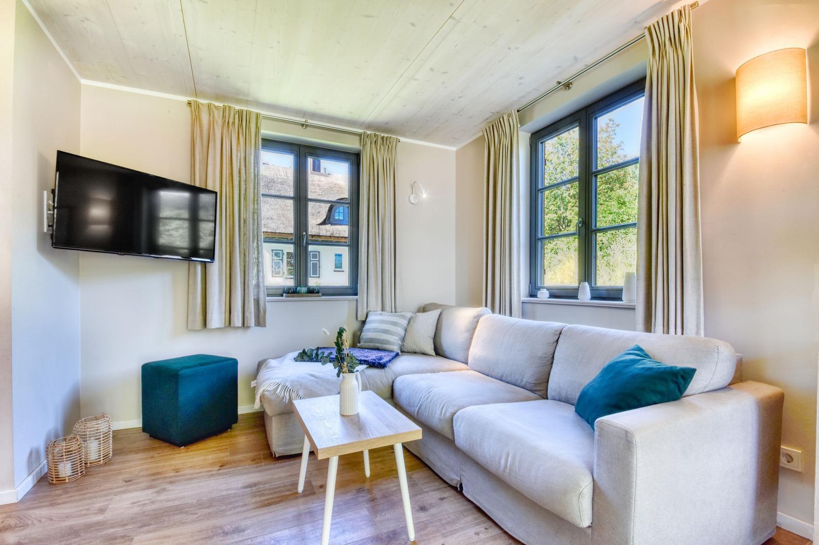Wohnzimmer mit Sofa, Fernseher und Fenstern mit Blick auf Dächer und Bäume.
