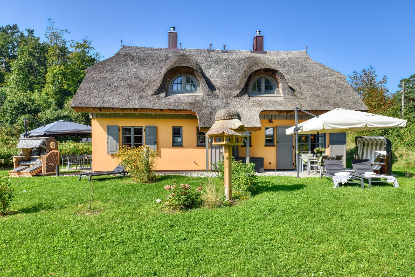 Haus mit Strohdach, Garten und Liegen unter Sonnenschirmen.