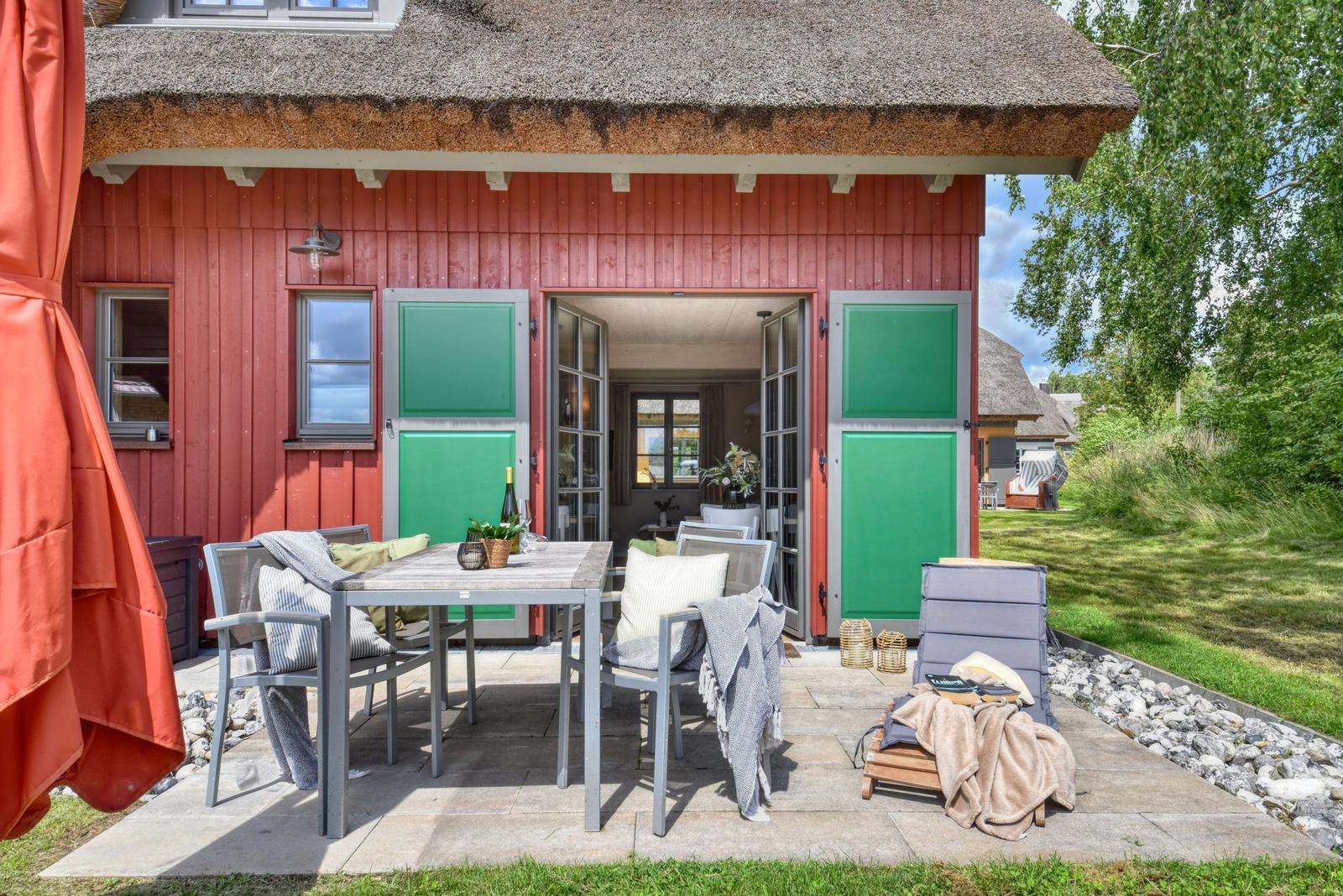 Roter Schuppen mit grünen Türen und Terrasse mit Tisch und Stühlen.
