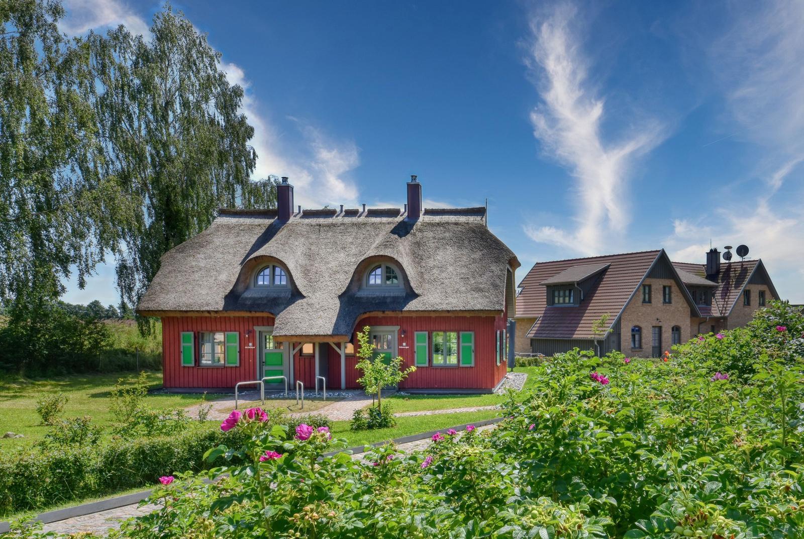 Rotes Haus mit Strohdach und grünen Fensterläden im Garten.