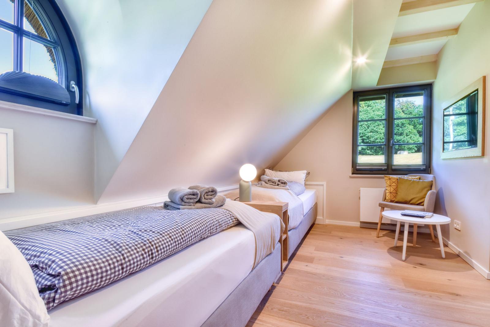 Zimmer mit zwei Betten, Holzboden und Fenstern zum Garten.