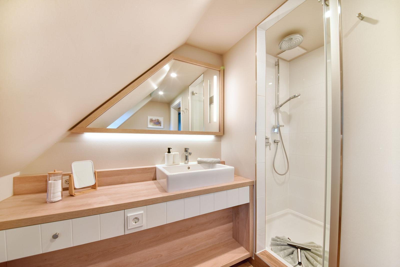 Badezimmer mit Dusche, Waschbecken und Spiegel unter Dachschrägen.