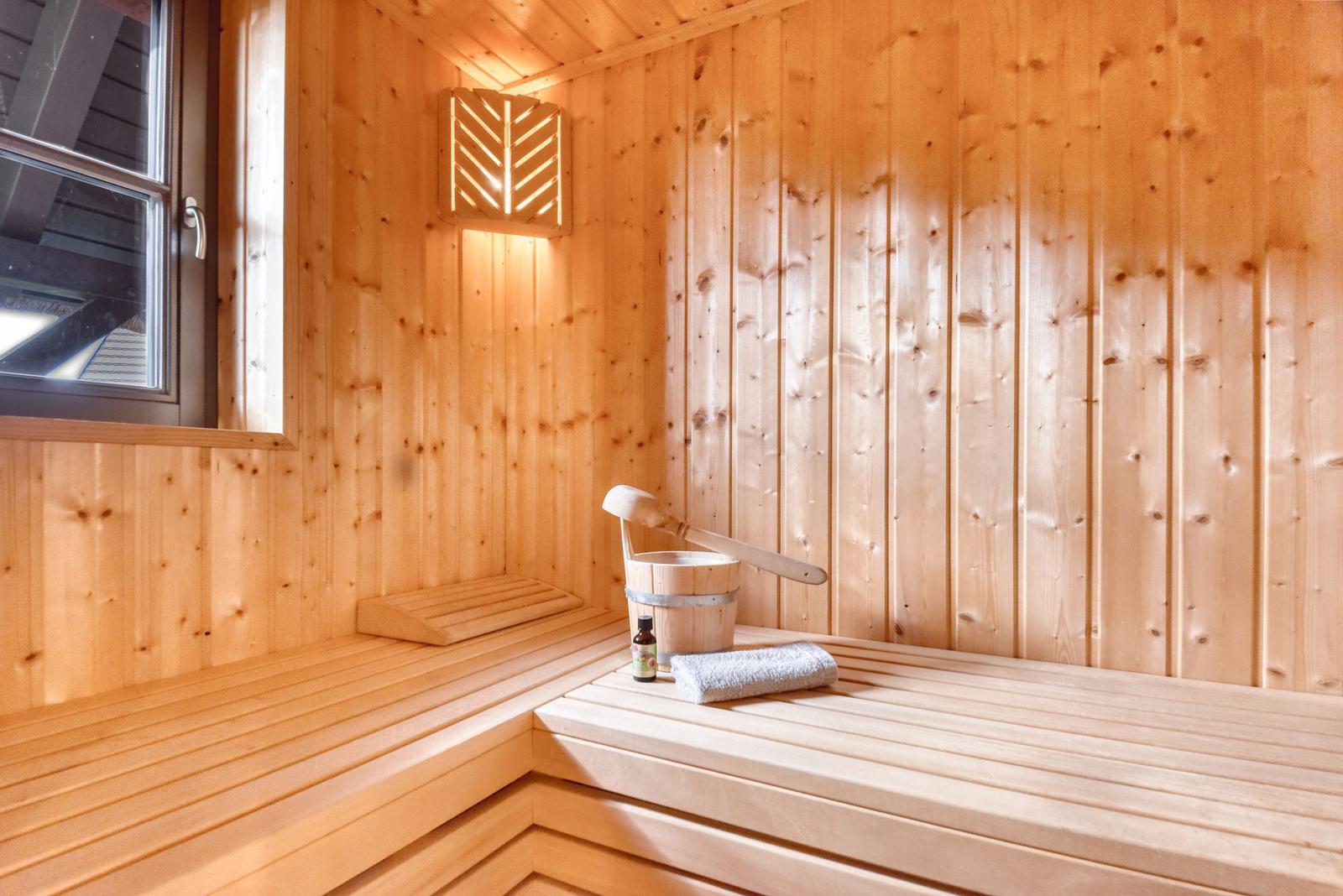 Sauna mit Holzwand, Sitzbank, Eimer und Handtuch.