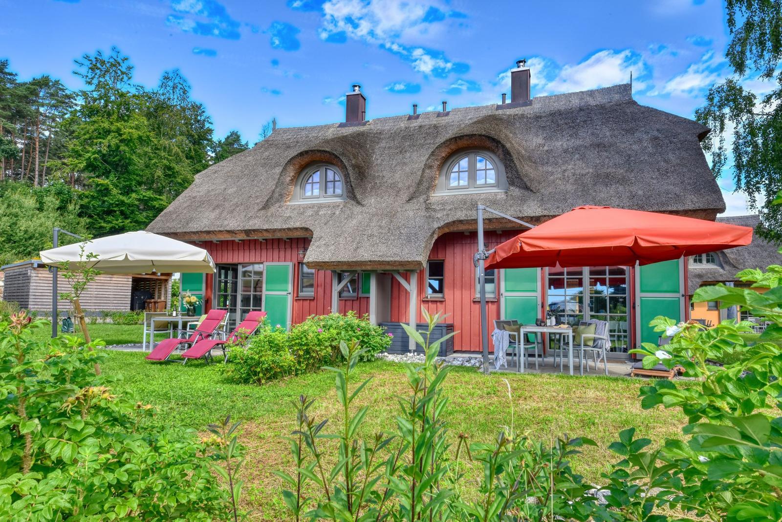 Rotes Haus mit Strohdach, Garten mit Sonnenschirmen und Liegestühlen.