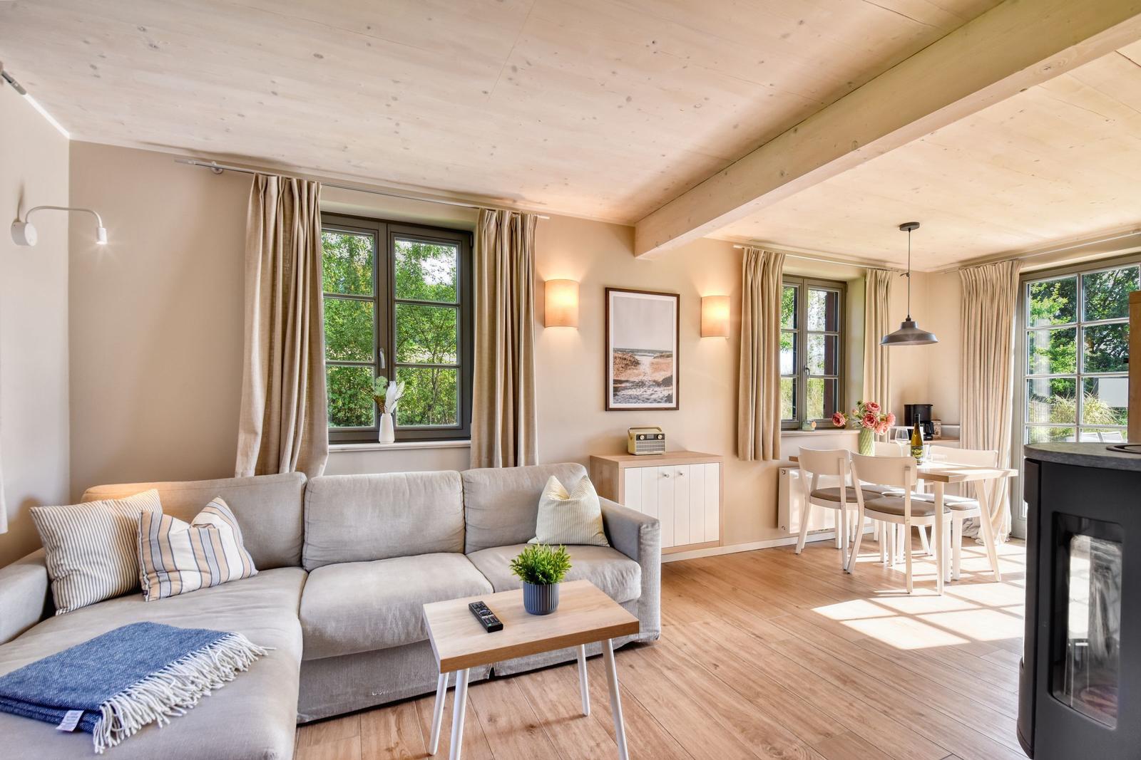 Wohn- und Essbereich mit Sofa, Tisch, Stühlen und Fenstern. Holzdecke und -boden.