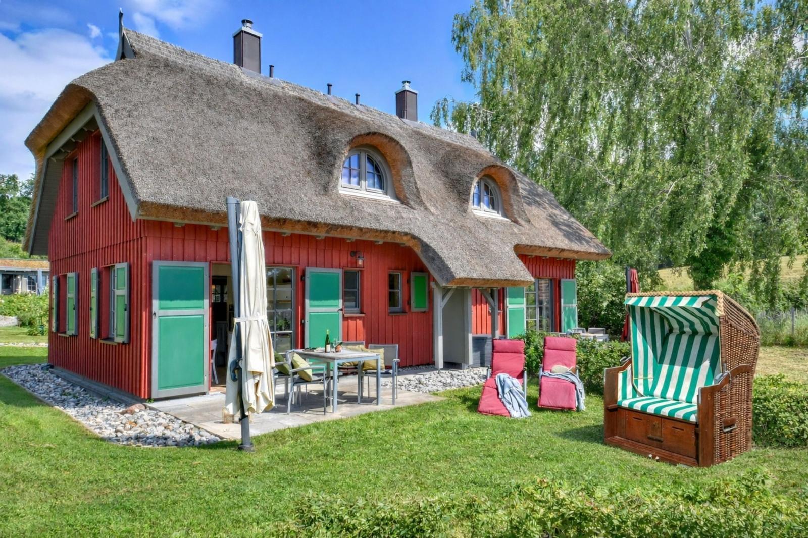 Rotes Haus mit Strohdach, Terrasse und Strandkorb im Garten.