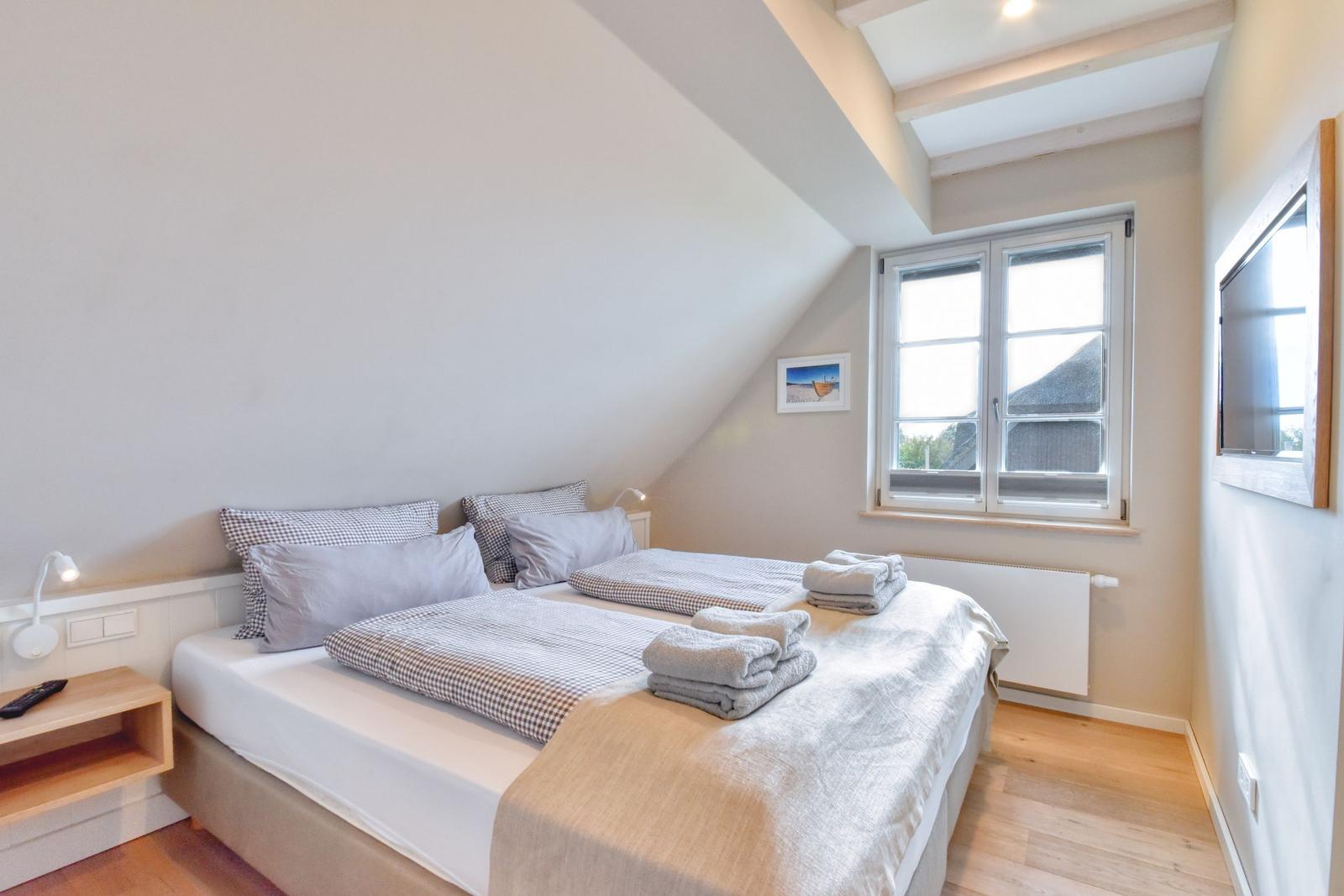 Schlafzimmer mit Doppelbett, Fenster und Fernseher an der Wand.