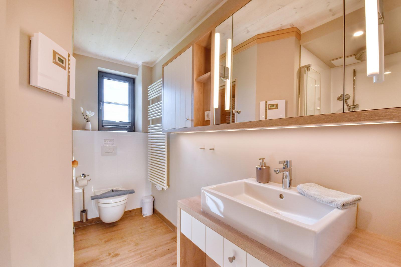 Badezimmer mit Waschbecken, Spiegel, Toilette und Fenster.