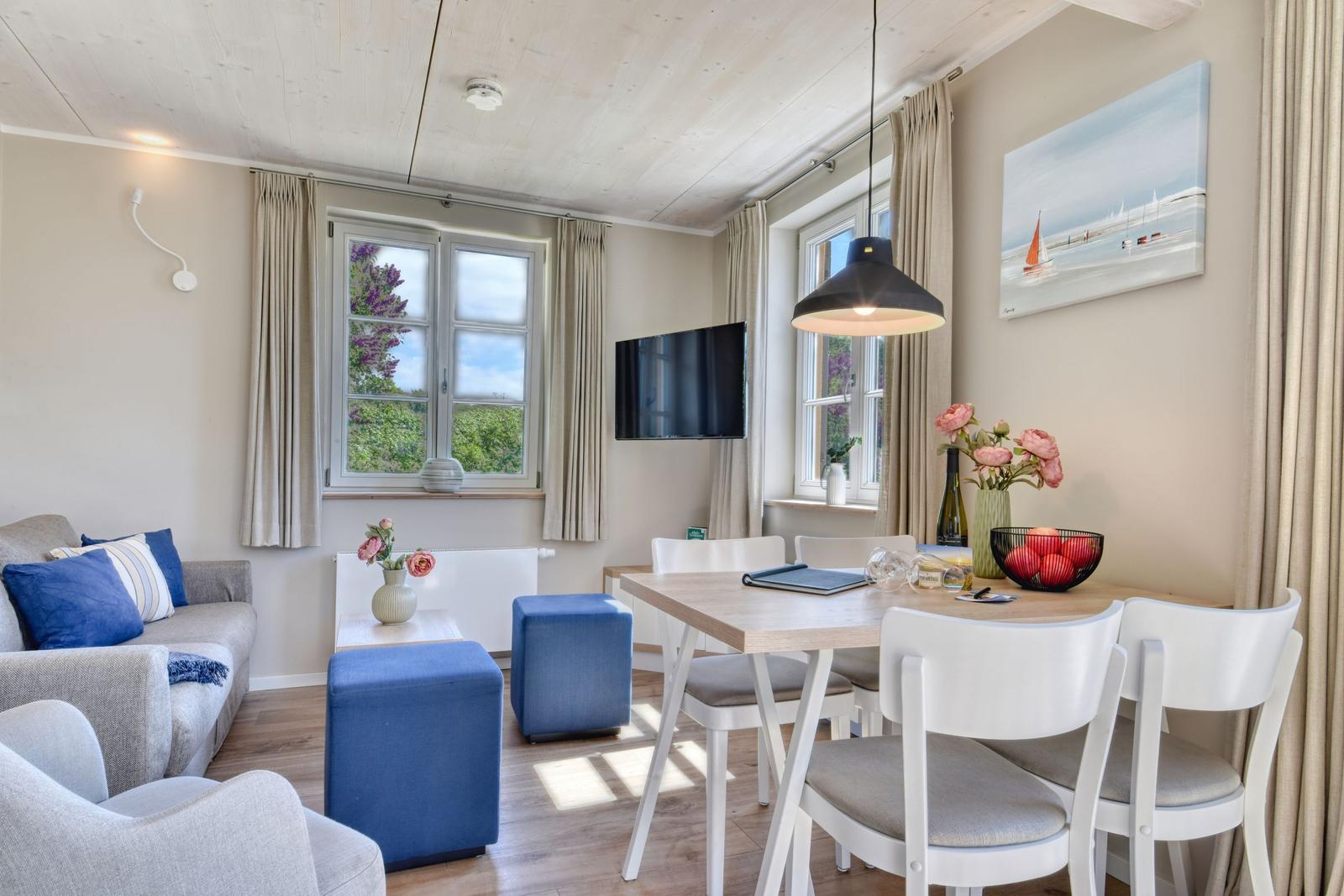 Wohn- und Essbereich mit Sofa, Esstisch und TV. Fenster mit Blick auf Grün.