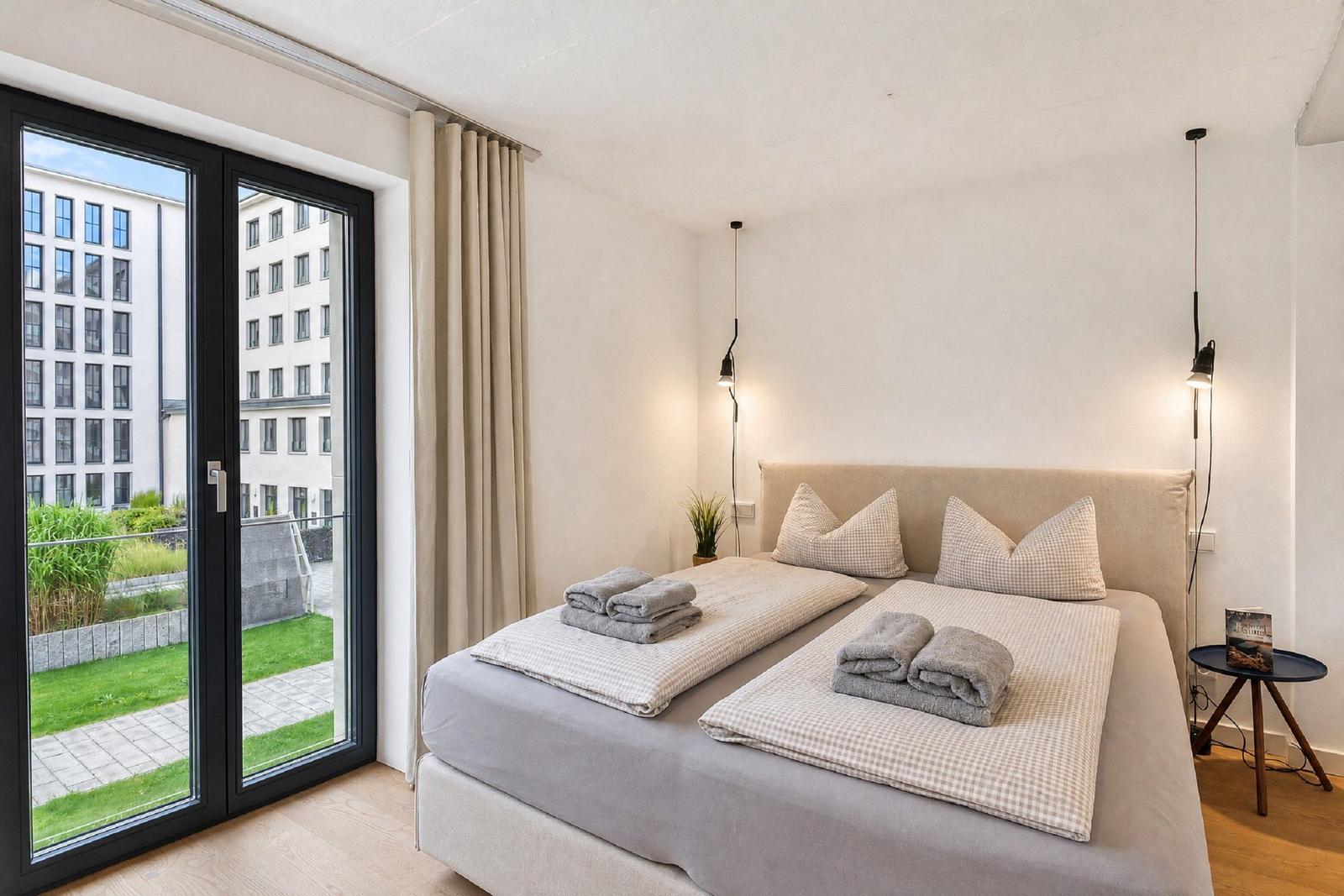 Schlafzimmer mit Doppelbett, Balkon und moderner Beleuchtung.