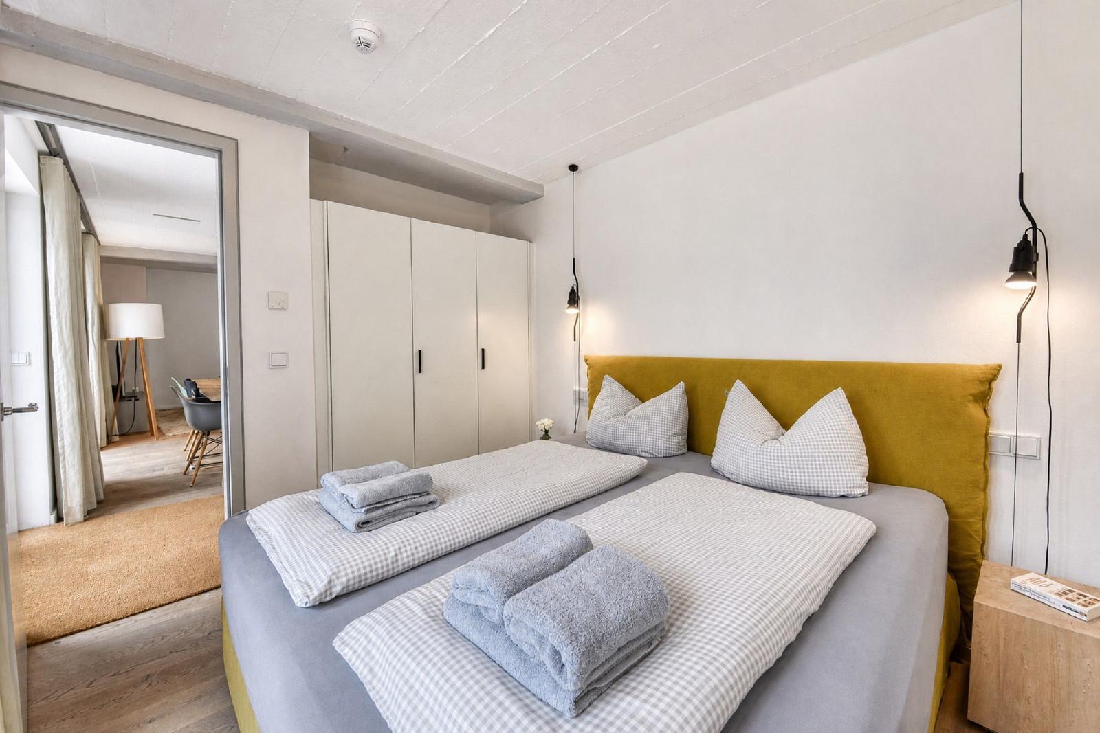 Schlafzimmer mit Bett, Kleiderschrank und Blick in angrenzenden Raum.
