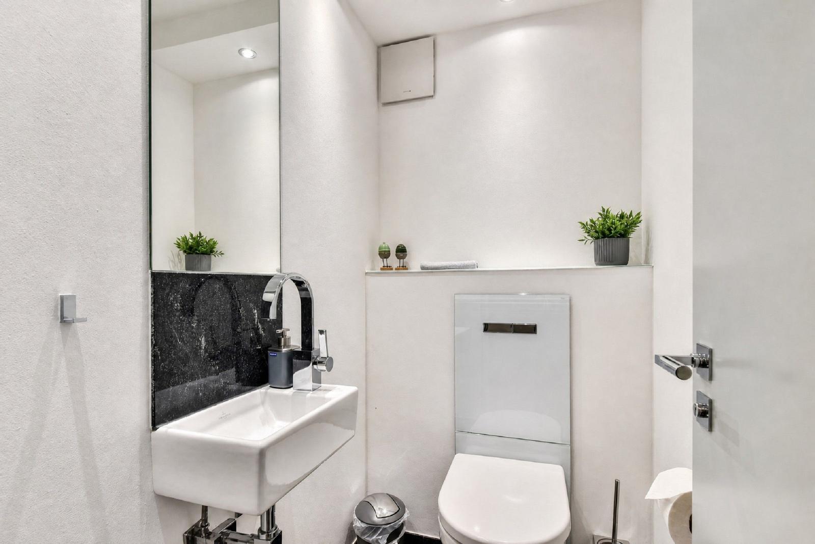 Badezimmer mit Waschbecken, Spiegel und Toilette. Weiße Wände und moderne Einrichtung.