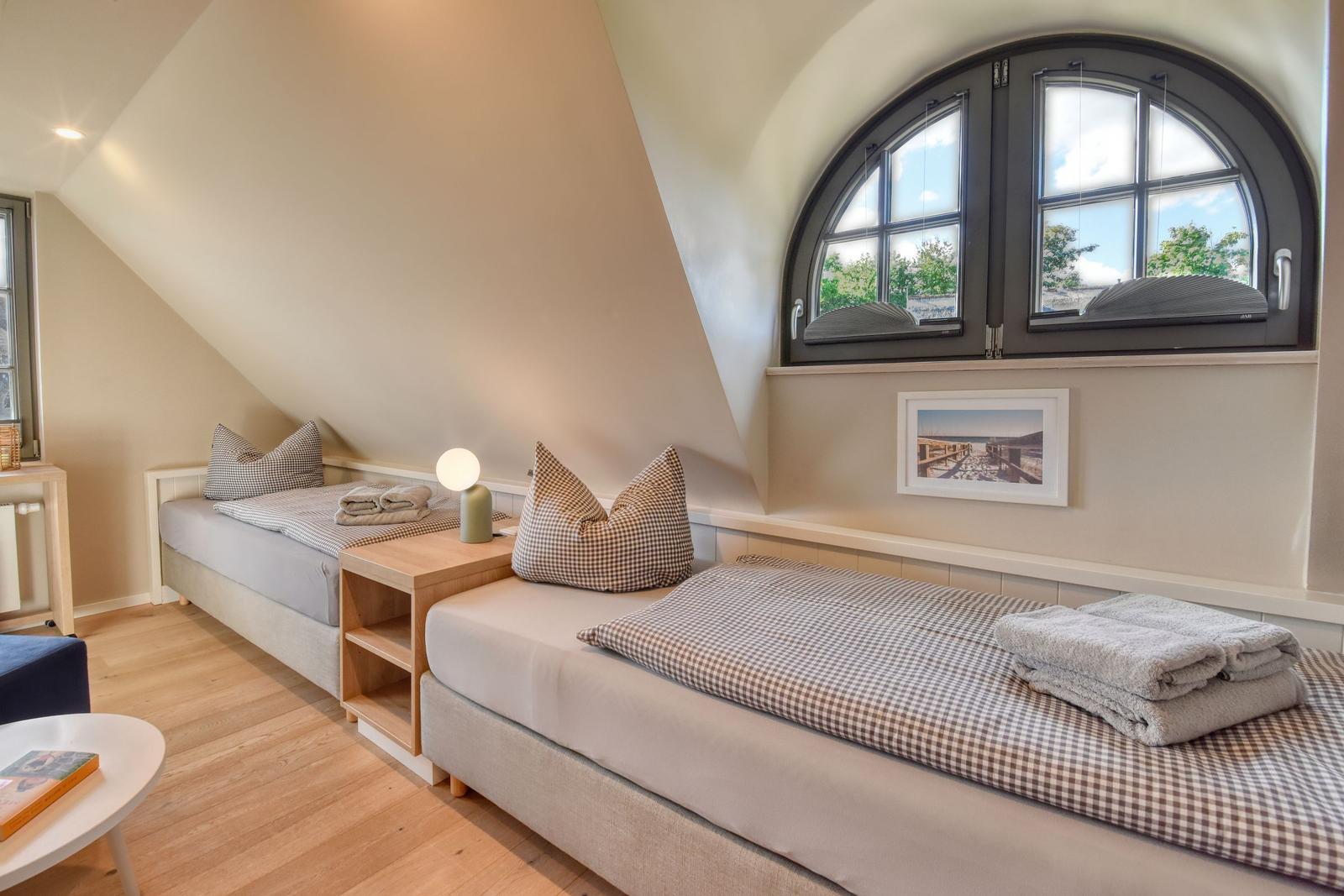 Two beds under sloped ceilings with wooden floor and large arched window.