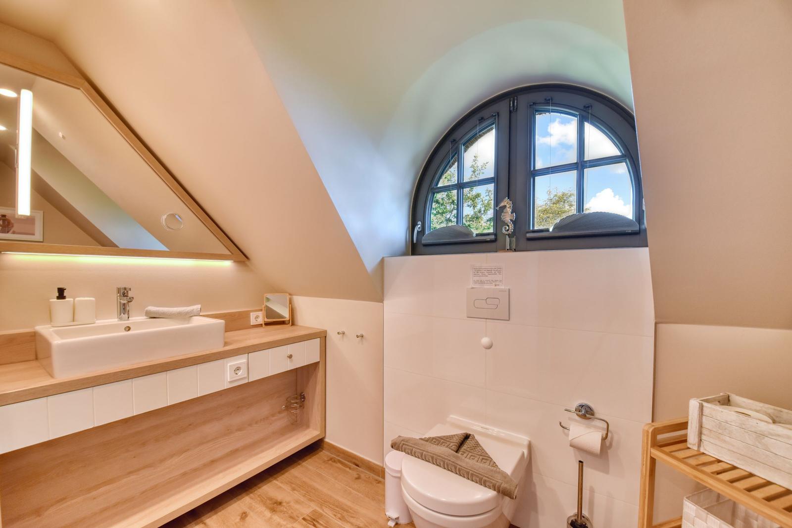 Bathroom with sink, toilet, and arched window. Wooden countertop and white tiled area.