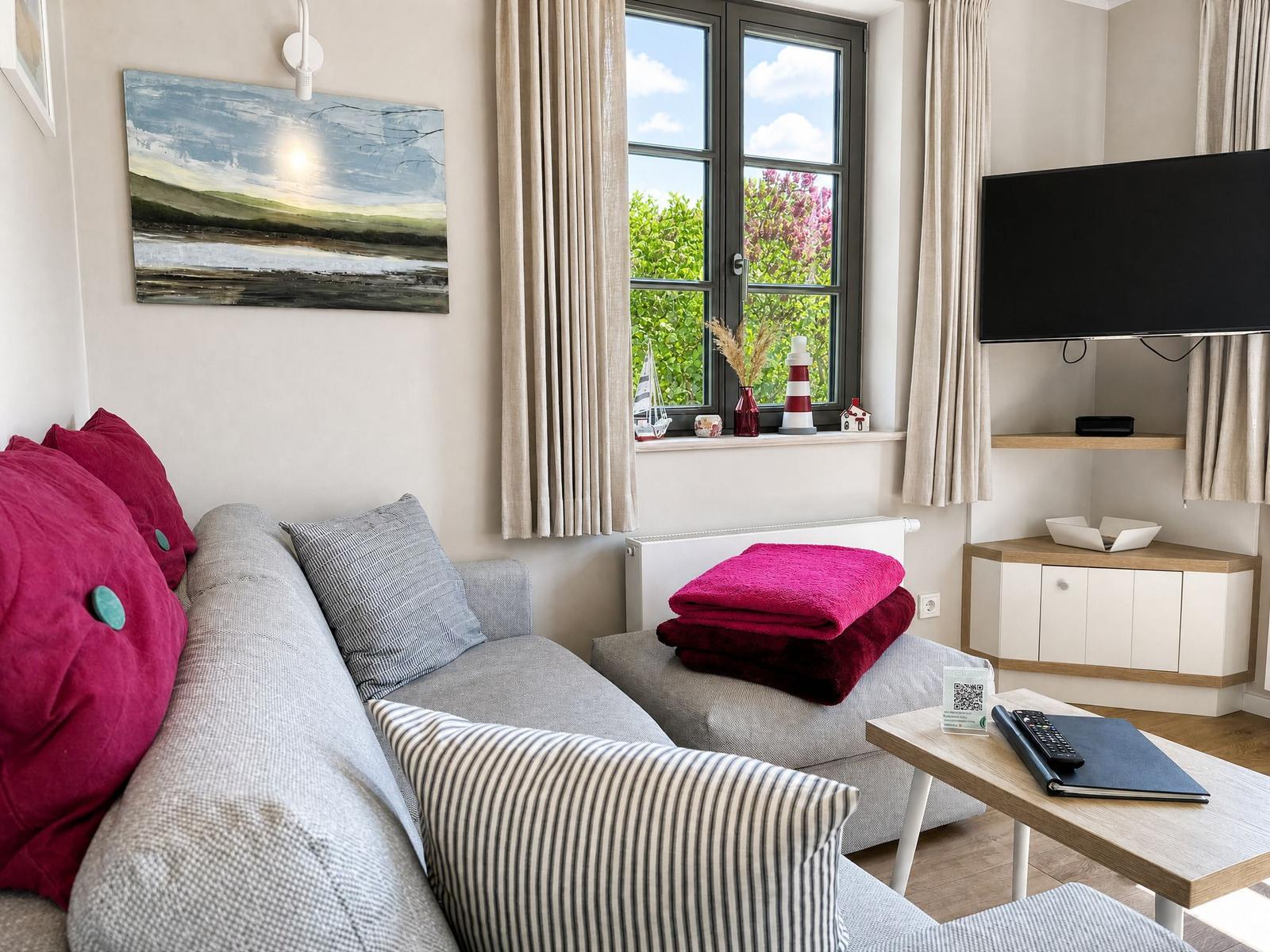 A living room with sofa, TV, and window view of greenery.