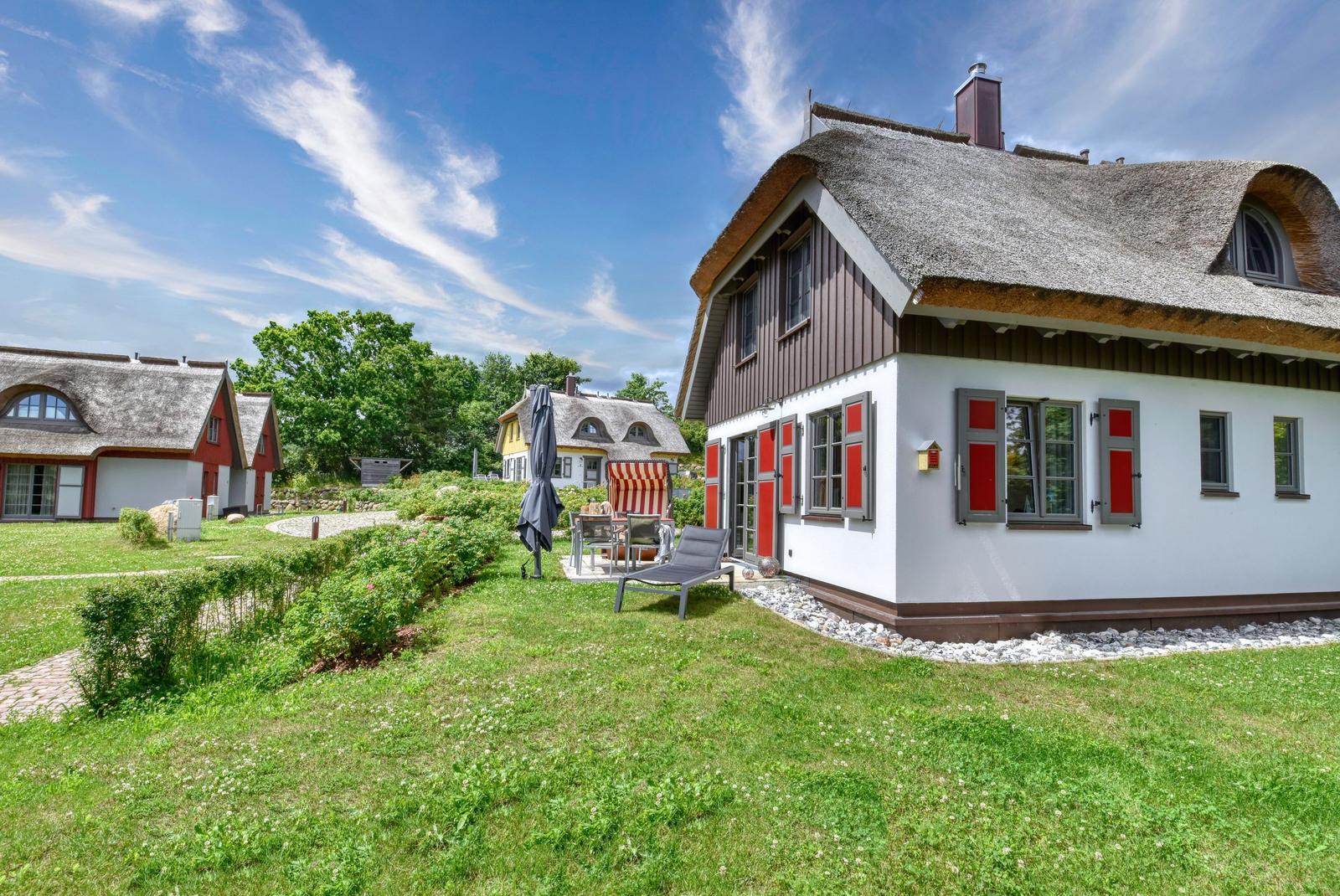 House with thatched roof, red shutters, and garden with lounge chair.
