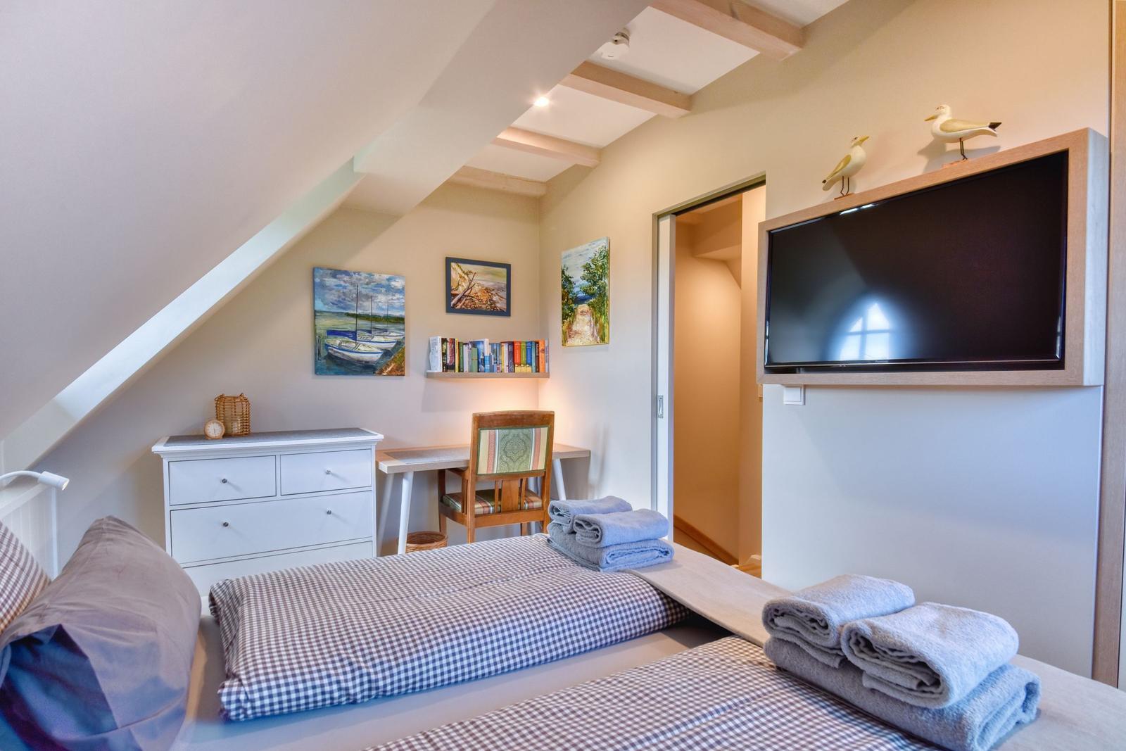 Schlafzimmer mit Doppelbett, Schreibtisch, Fernseher und Wandbildern.