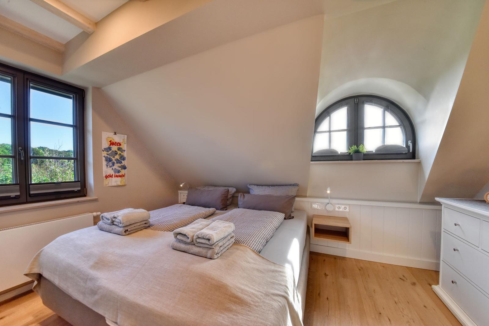 Schlafzimmer mit Doppelbett, Holzboden und zwei Fenstern mit Blick auf die Landschaft.