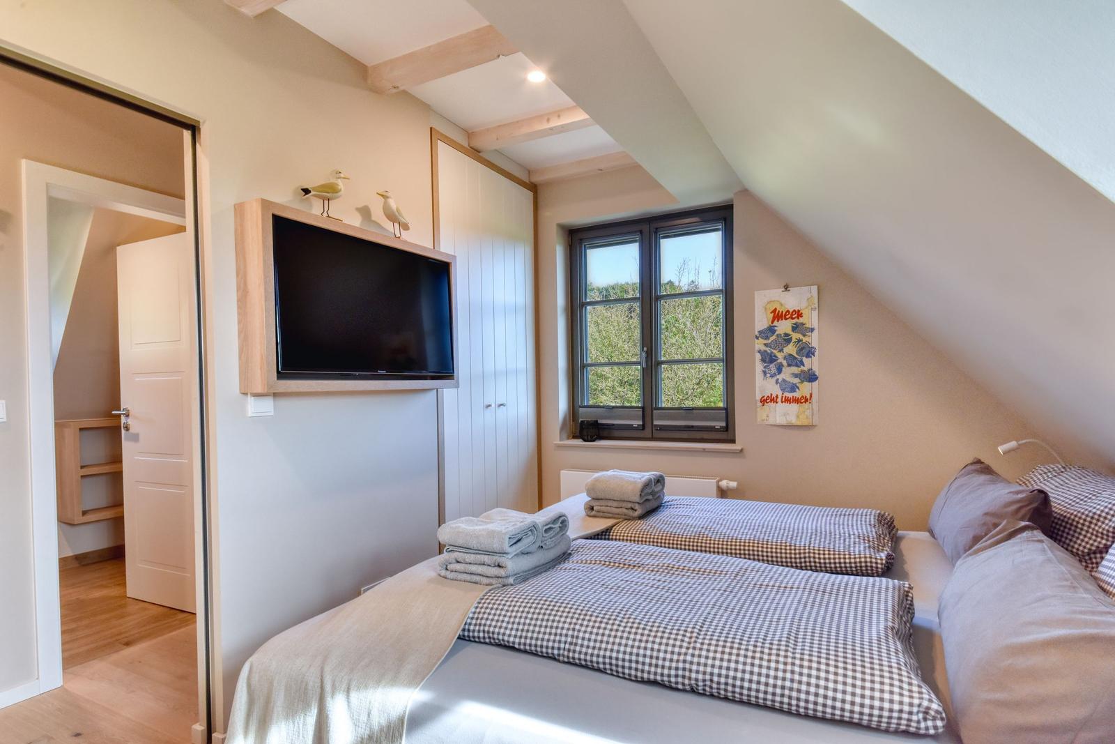 Schlafzimmer mit Doppelbett, TV und Fenster. Blick auf grüne Landschaft.