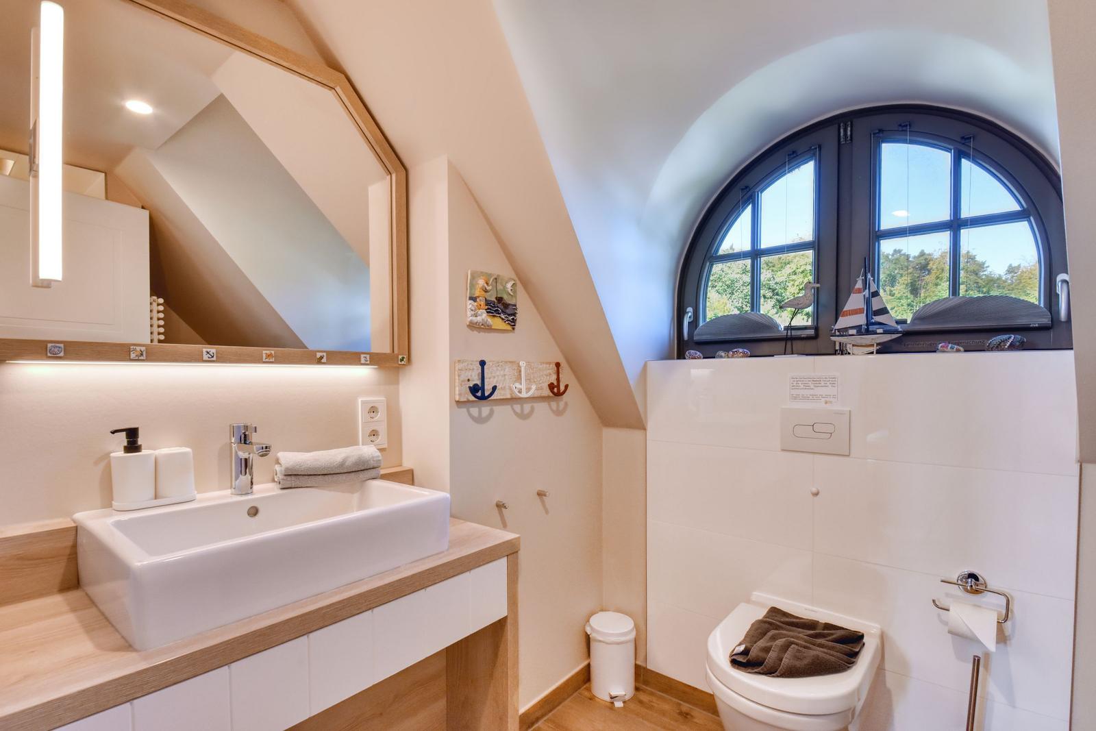 Badezimmer mit Waschbecken, Spiegel und Toilette unter einem Bogenfenster.