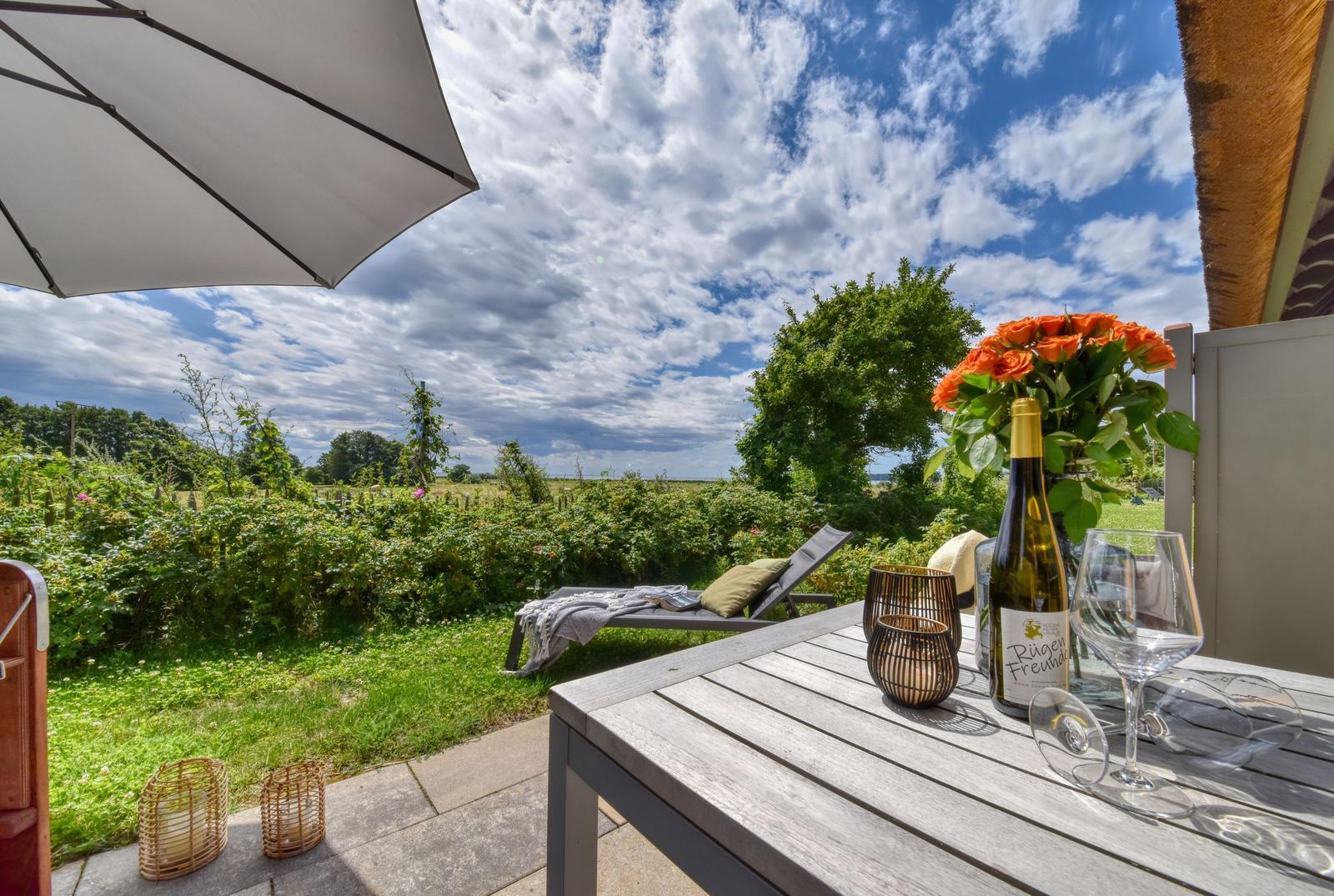 Terrasse mit Tisch, Sonnenschirm und Blick auf grüne Wiesen.