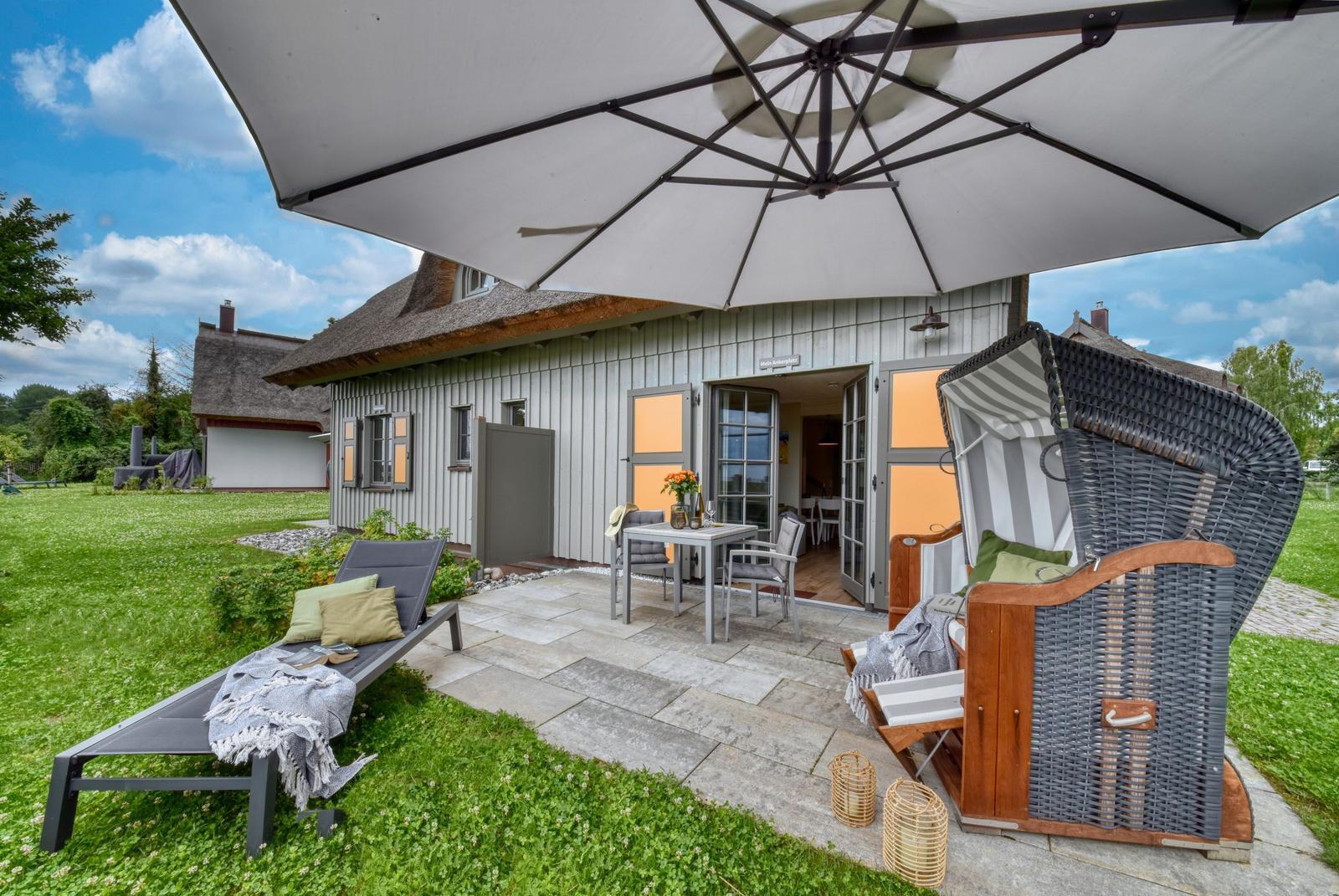 Terrasse mit Sonnenschirm, Liegestuhl und Strandkorb vor einem Haus mit Schiebetüren.