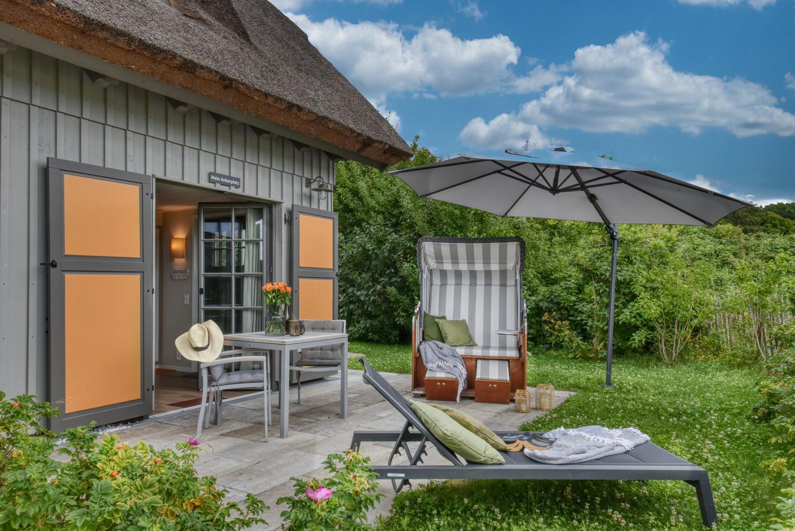 Haus mit Terrasse, Liegestuhl und Strandkorb unter Sonnenschirm.