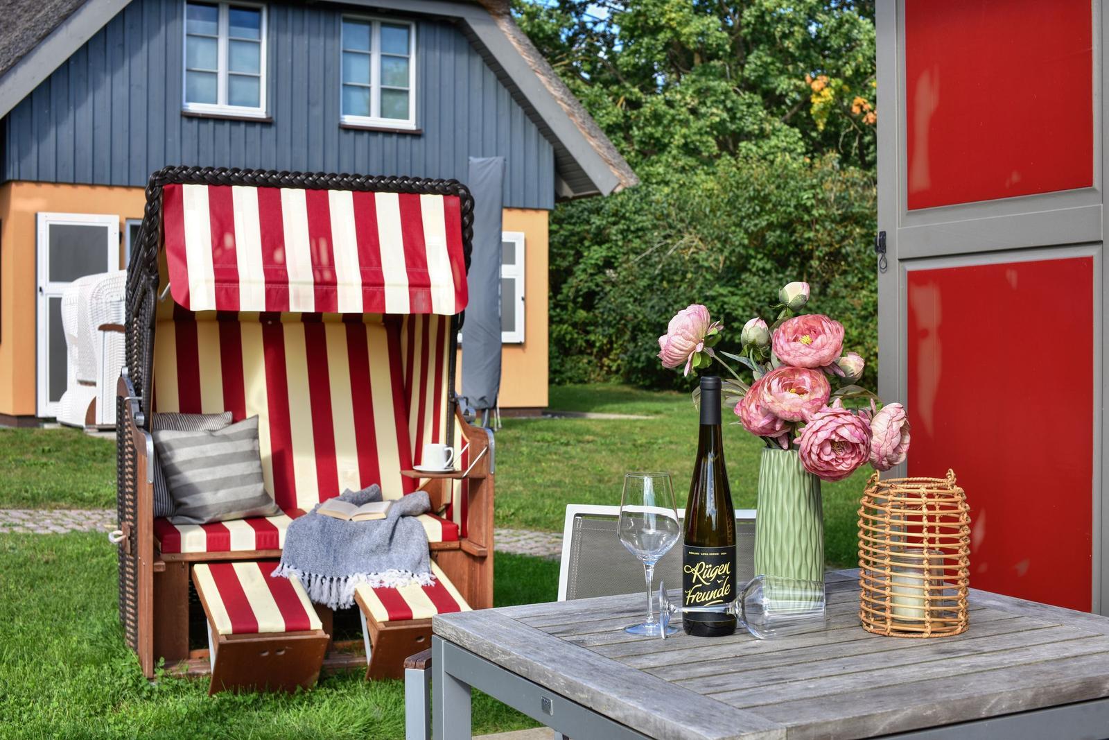 Red beach chair with table, wine, and flowers in the garden in front of a house.